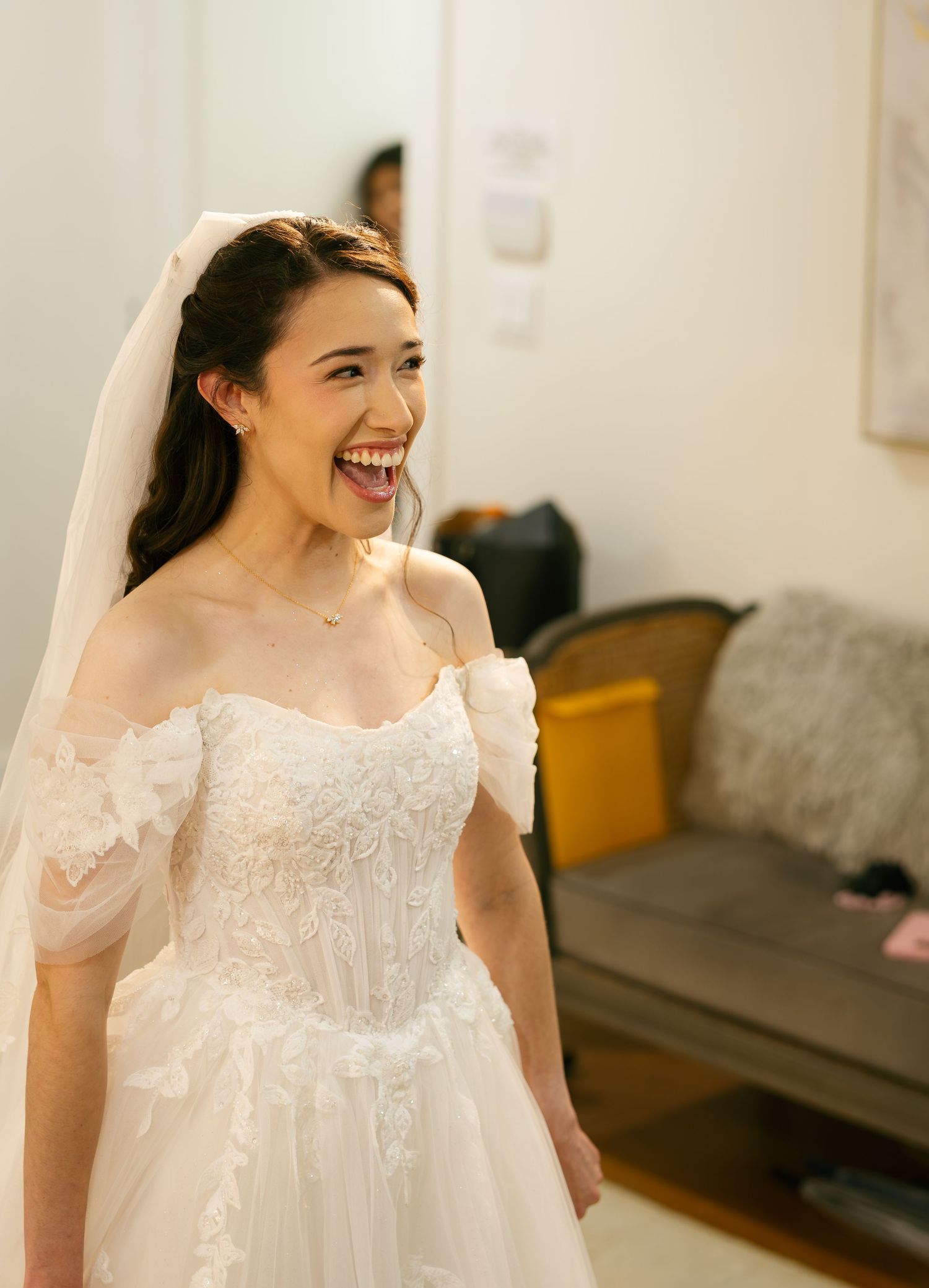 Joyful bride in an off-shoulder lace wedding gown and veil laughing radiantly on her wedding day.