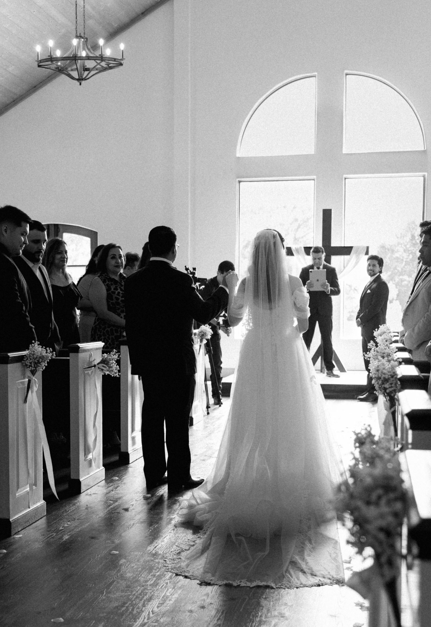 Black and white photo of bride walking down the aisle in a chapel wedding ceremony.