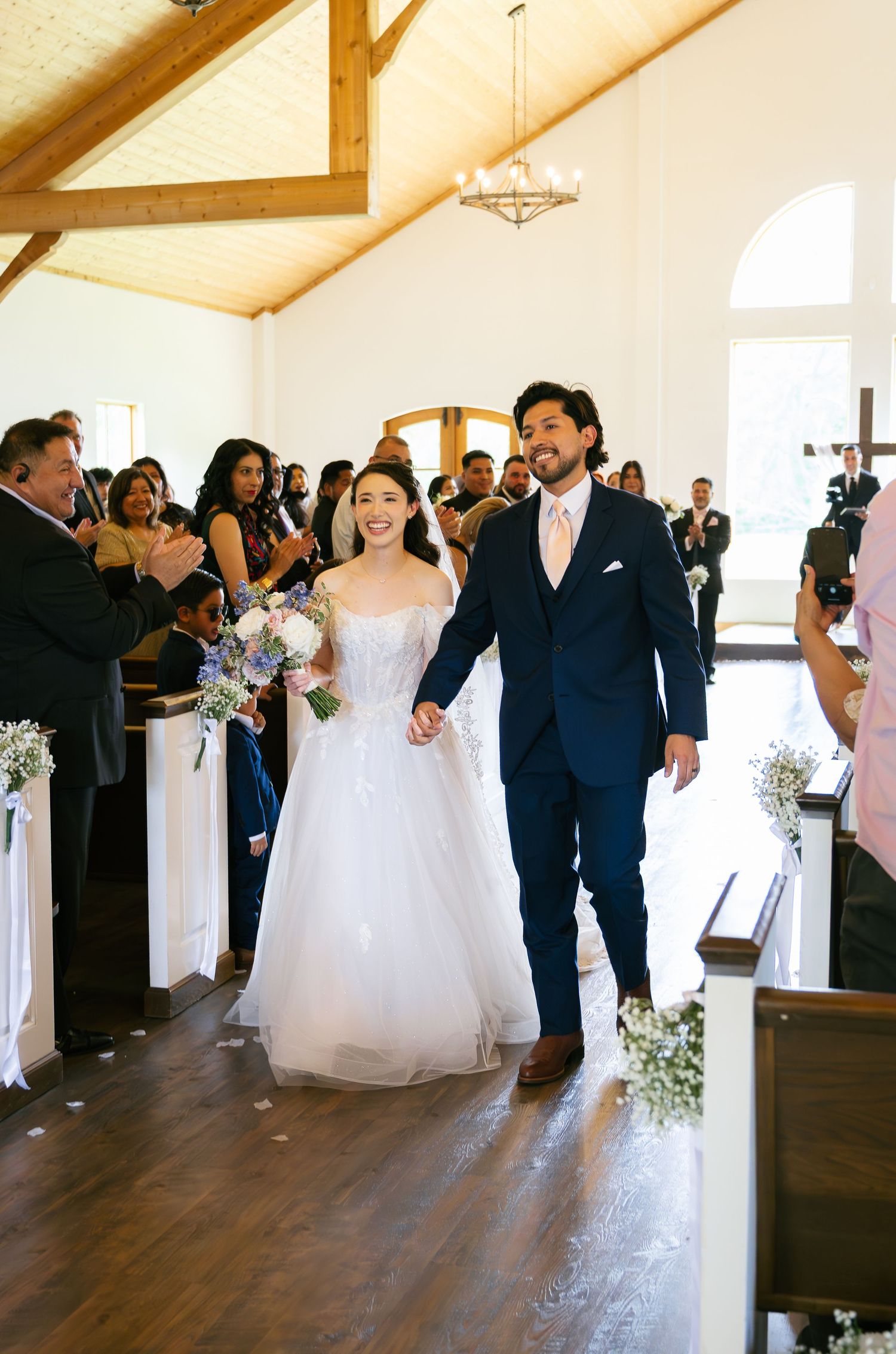 Smiling bride and groom walk down church aisle after wedding ceremony, bride holding bouquet.