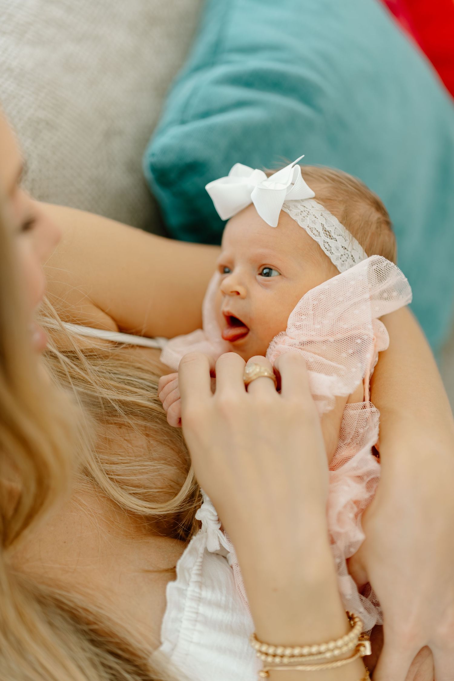 Mother holding newborn baby girl in pink ruffled dress and white bow headband, looking at each other lovingly.