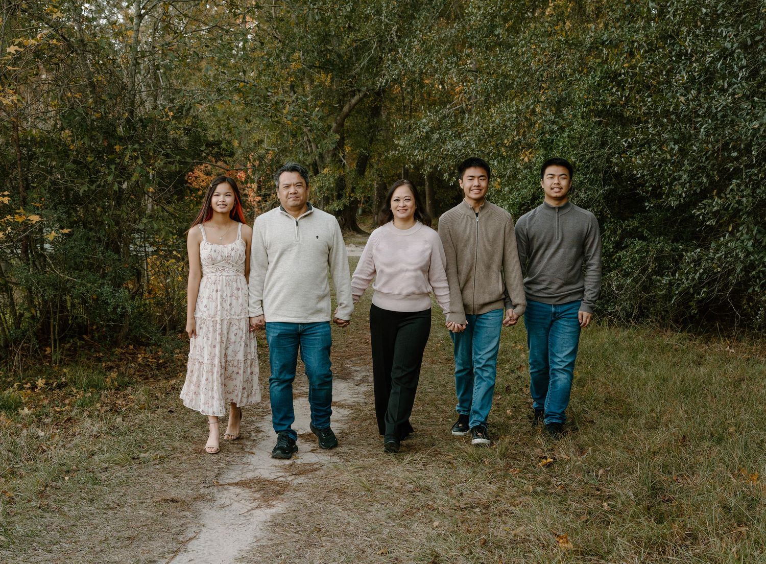 Family of five walking together on a wooded path surrounded by autumn foliage for a fall family portrait.
