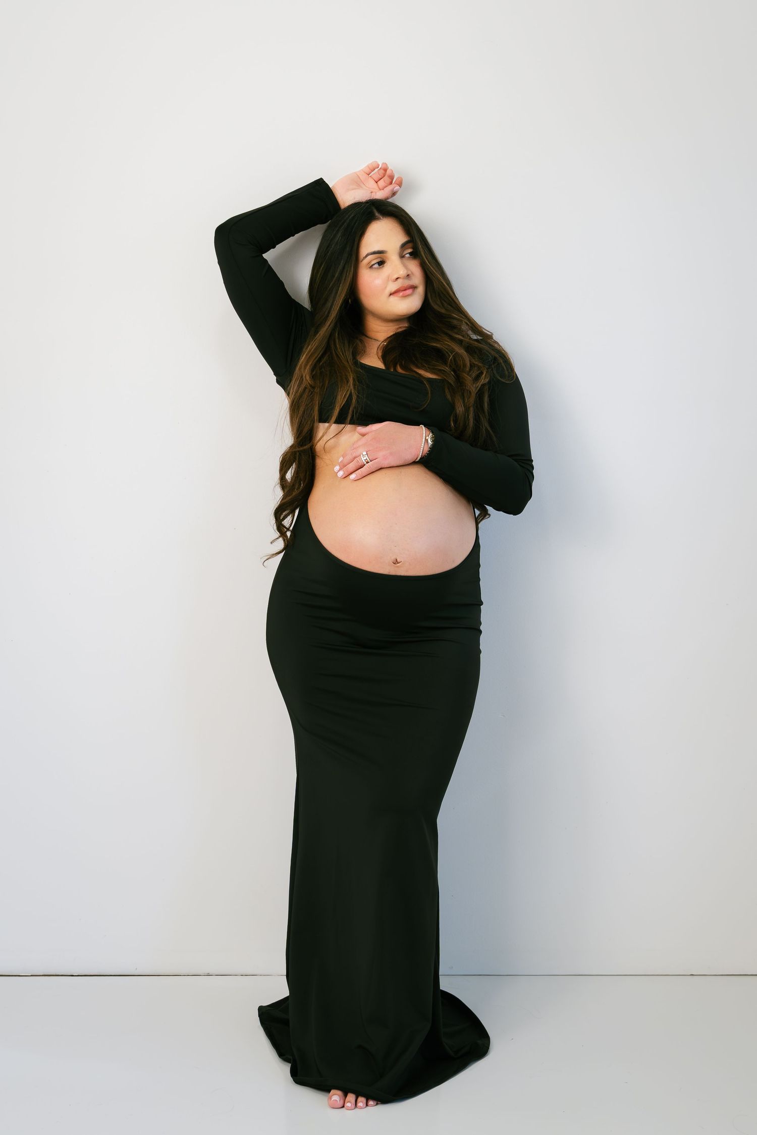 Pregnant woman in black crop top and maxi skirt cradling baby bump during maternity photo session.