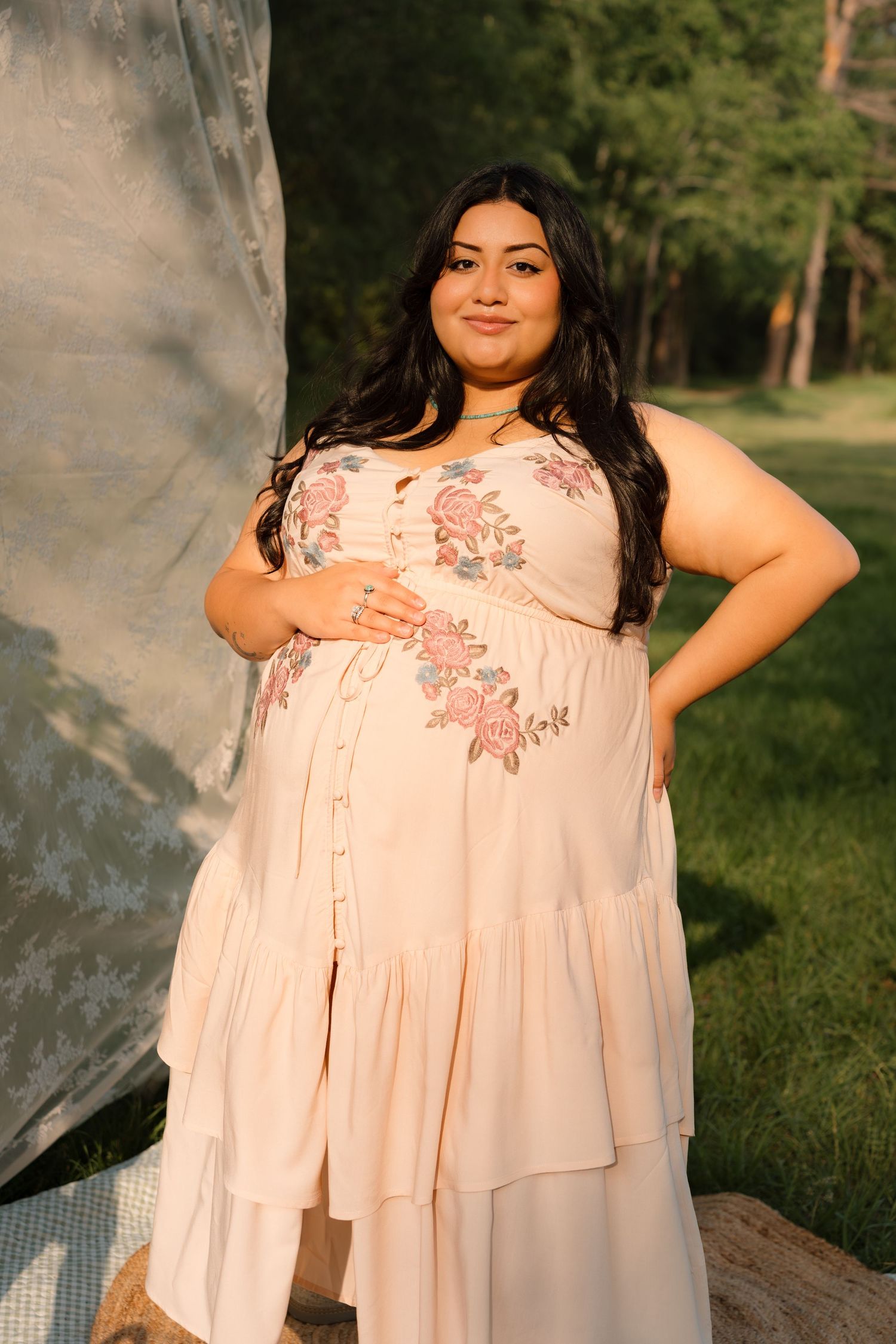 Woman in floral embroidered blush maxi dress posing outdoors in a park during golden hour.