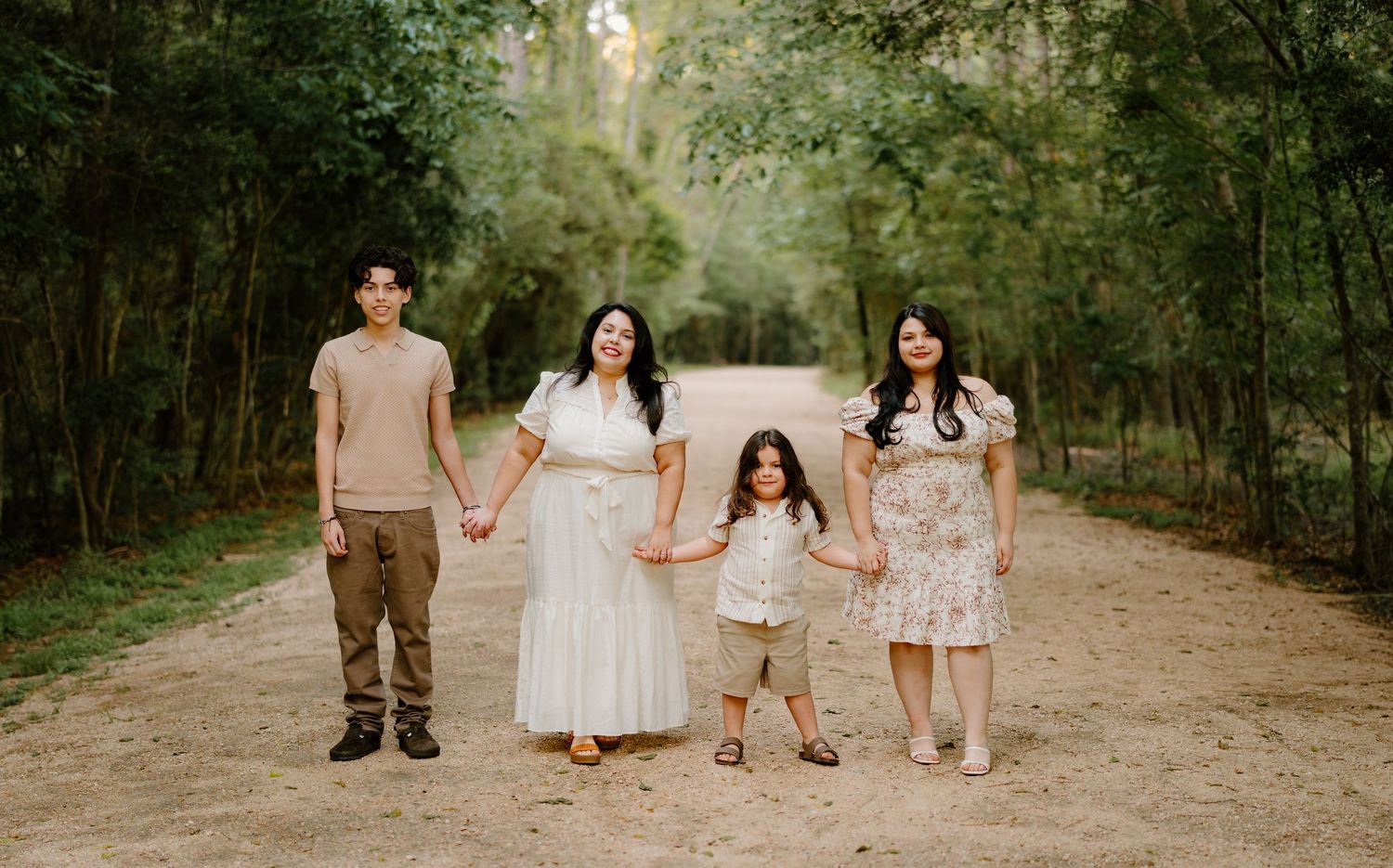 Family of four posing on a dirt path surrounded by lush green trees in a serene outdoor setting.