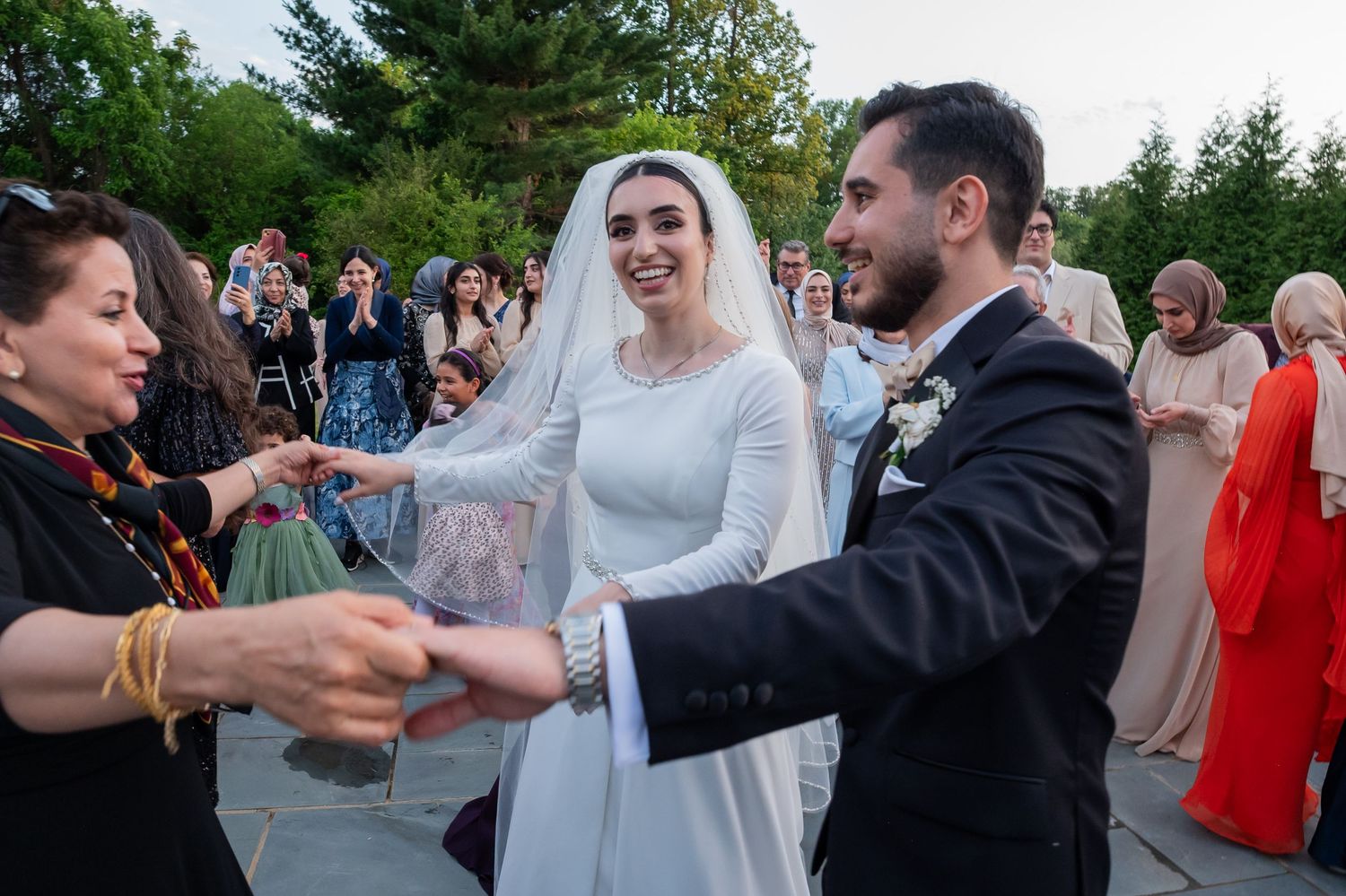 Bride in white gown and groom exchange gifts with guests at an outdoor wedding ceremony.