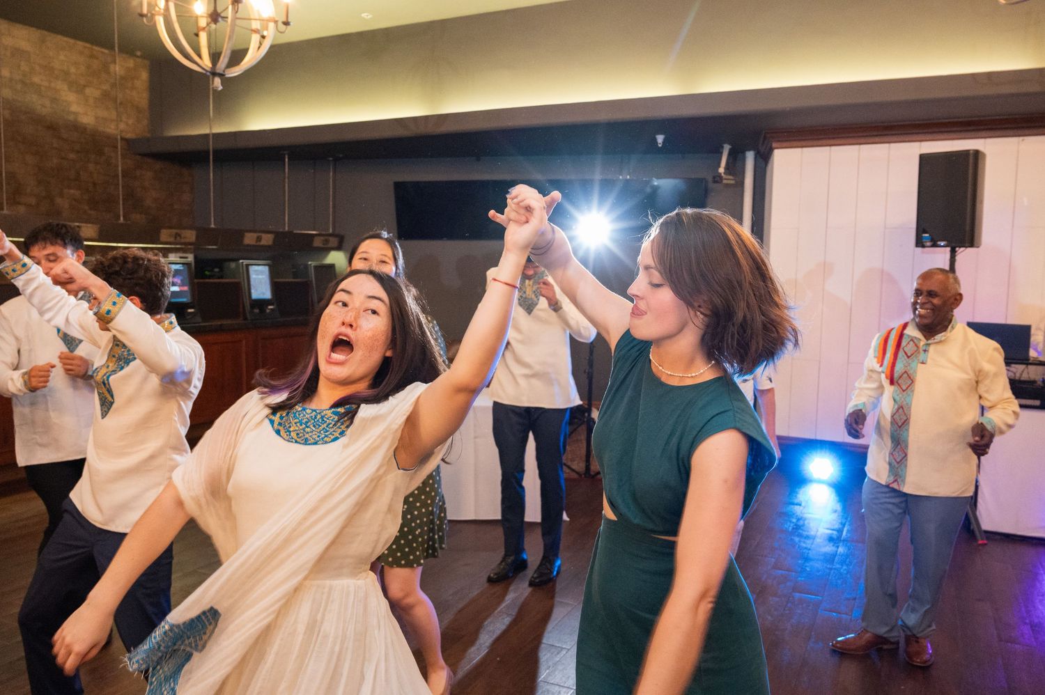 Guests dancing joyfully at a wedding reception, with a woman in white laughing while spinning on the dance floor.