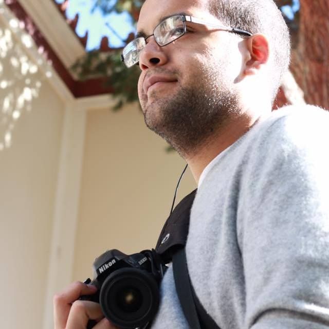 Male wedding photographer with glasses and Nikon camera looking up outdoors in natural light.