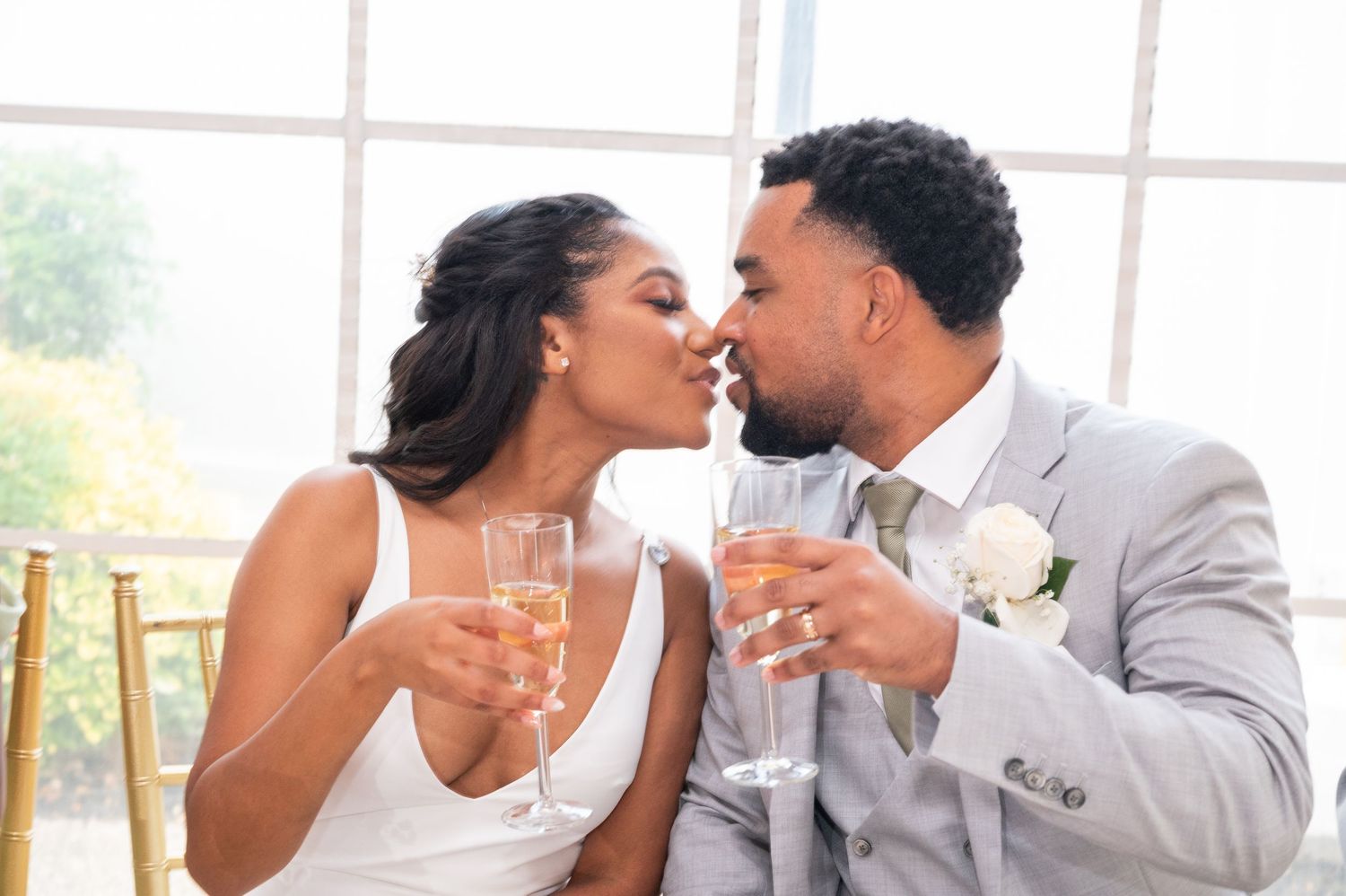 Newlywed couple sharing a romantic kiss while holding champagne glasses at their wedding reception.