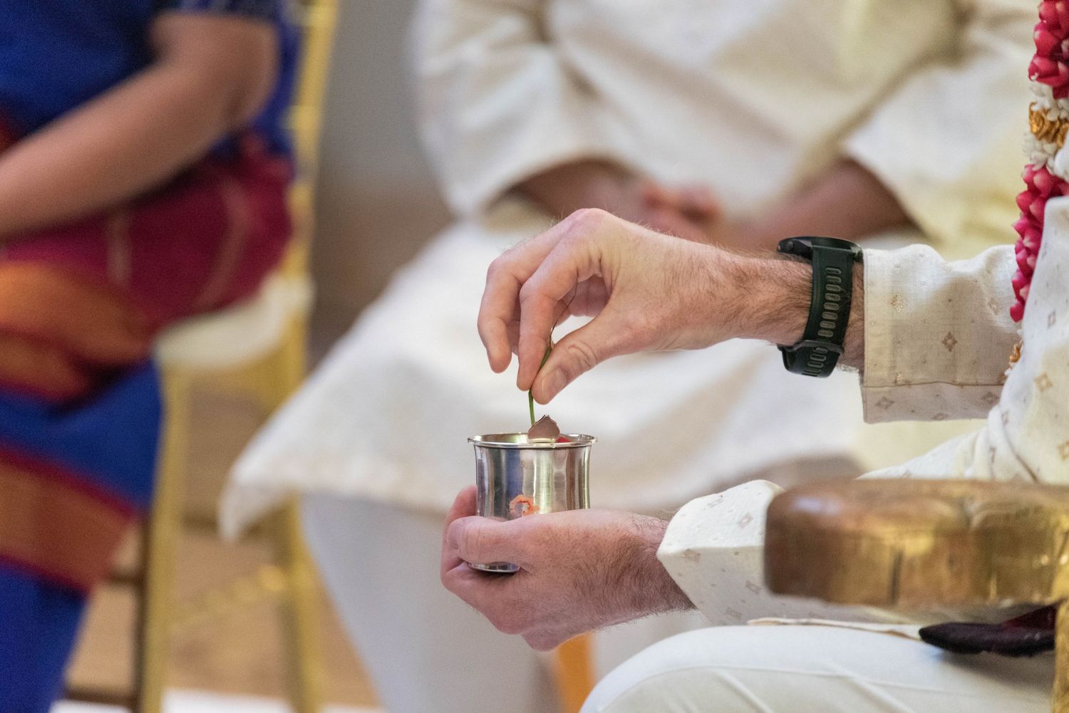 Elderly man performing traditional Indian wedding ritual with silver cup during Hindu ceremony indoors.