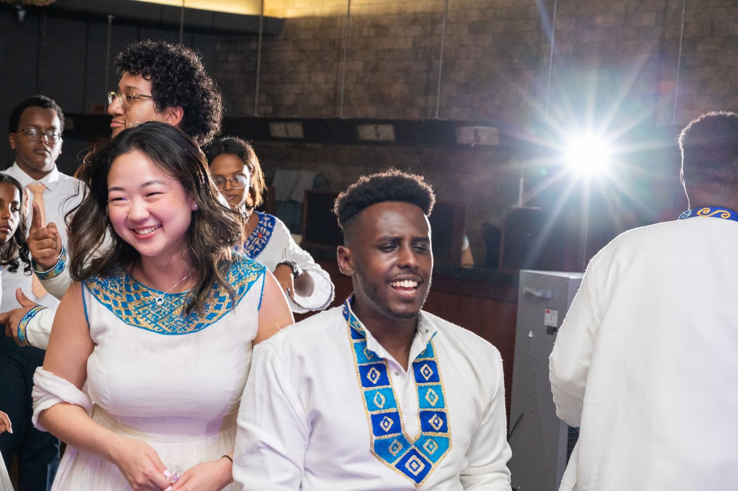 Couple in traditional African attire smiling at a cultural celebration event with bright lights in background.