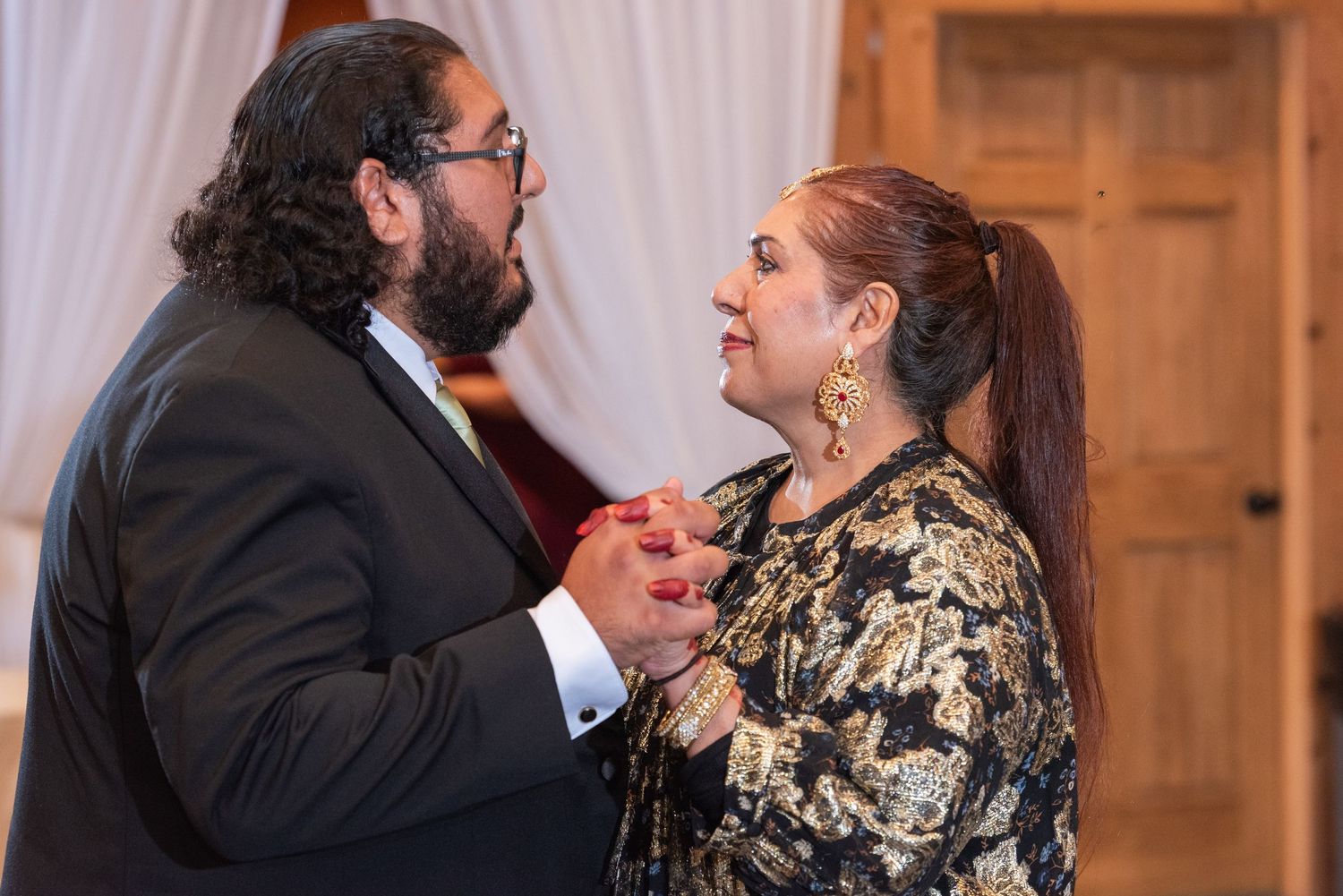 Man and woman in elegant attire share romantic dance moment at wedding reception indoors.