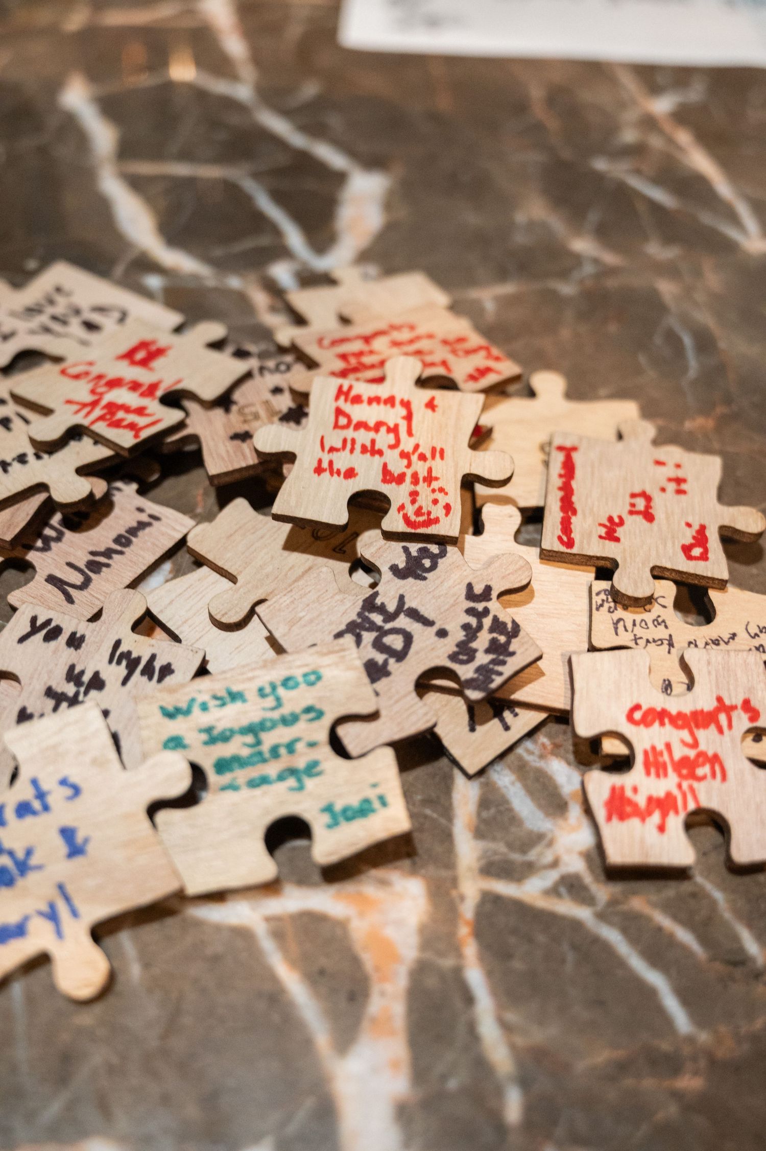 Wooden puzzle pieces with handwritten wedding guest messages and congratulations scattered on a marble surface.