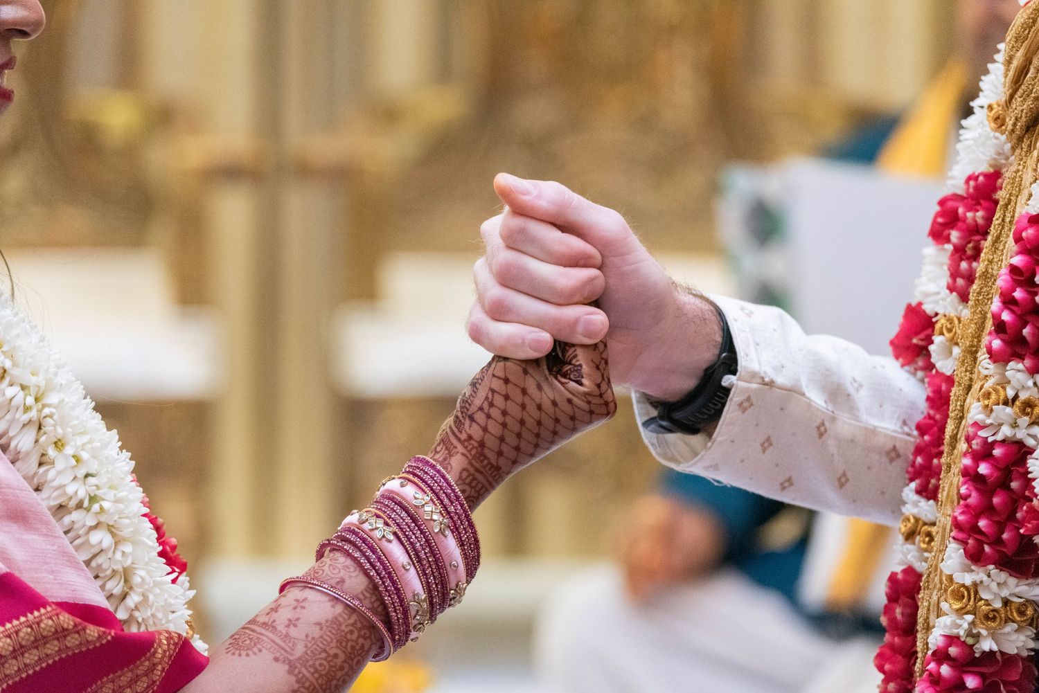 Indian bride and groom holding hands during traditional Hindu wedding ceremony with henna and bangles.