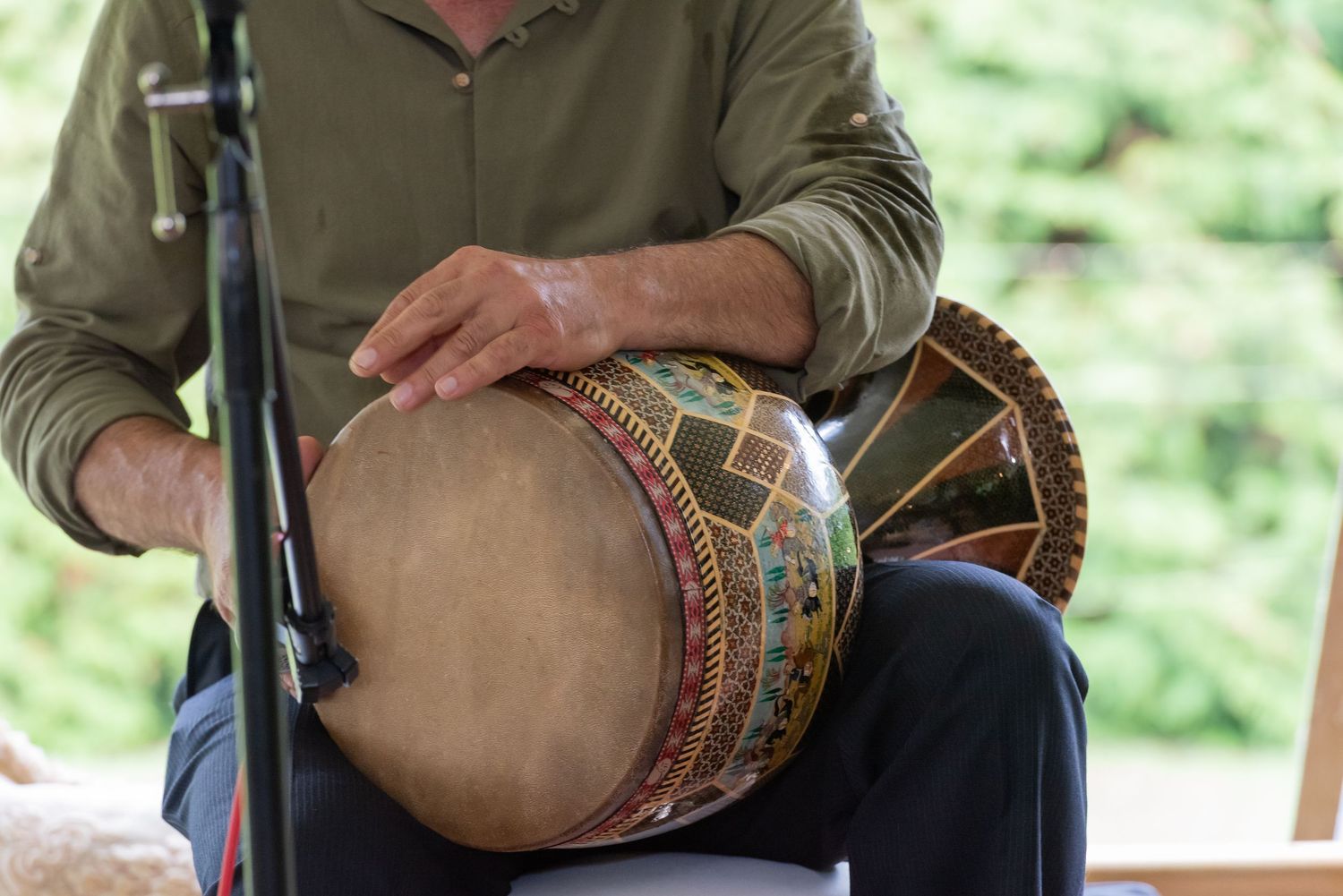 Man playing a decorative djembe drum outdoors, hands resting on the colorful hand drum during a performance.