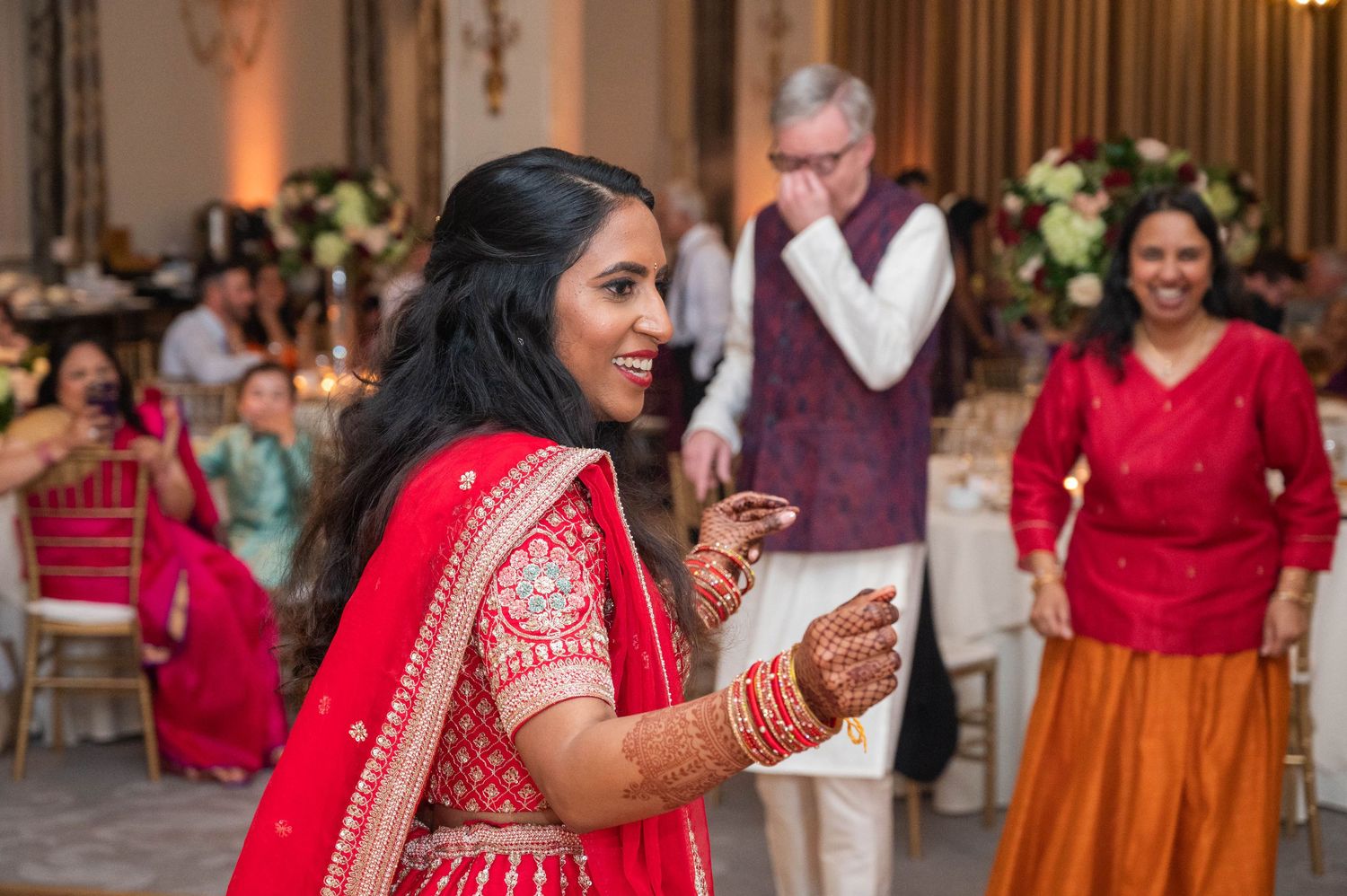 Indian bride in red lehenga with mehndi dancing joyfully at wedding reception celebration.