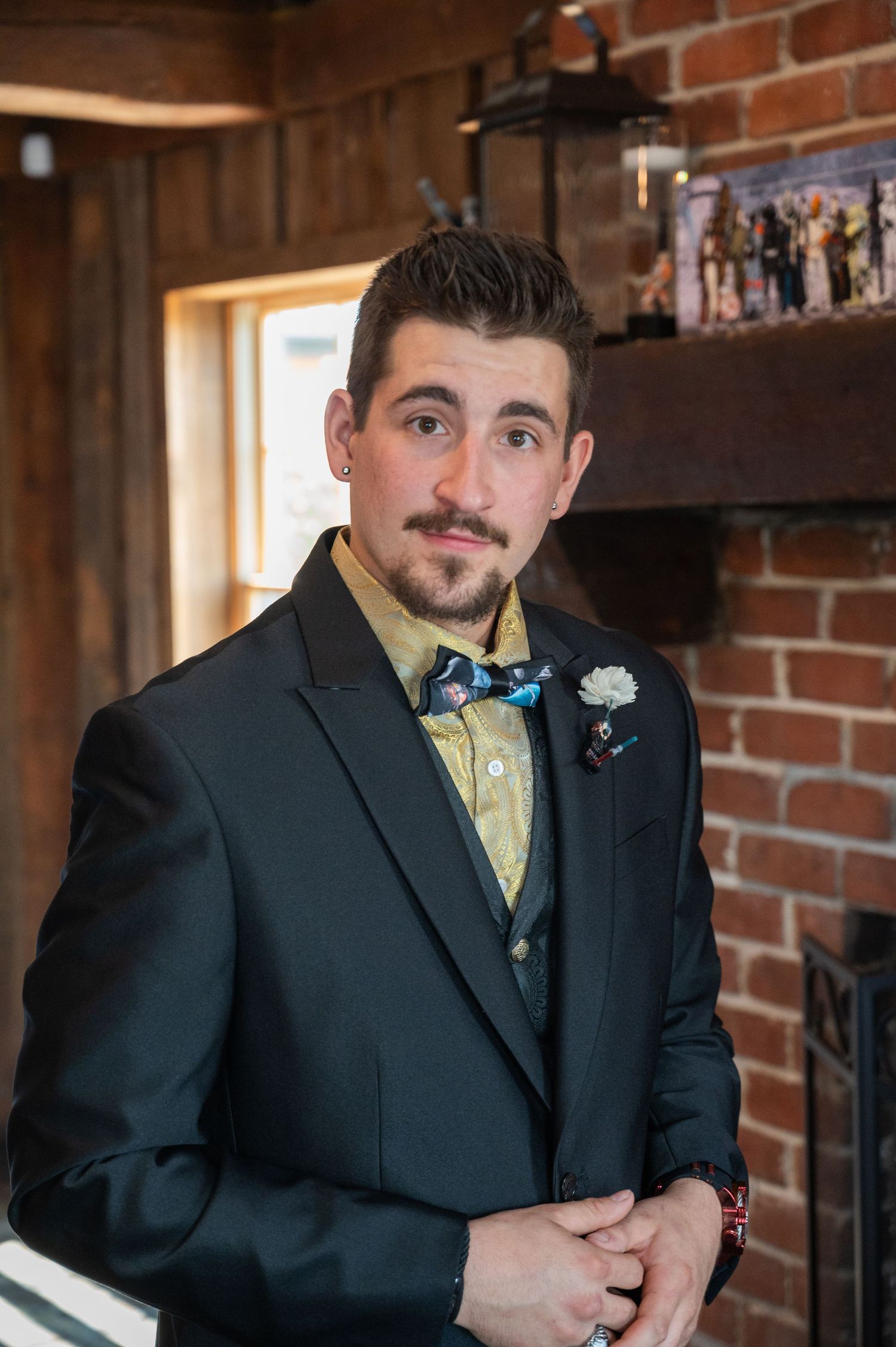 Groom in black suit with gold shirt and blue bow tie wearing a white boutonniere.