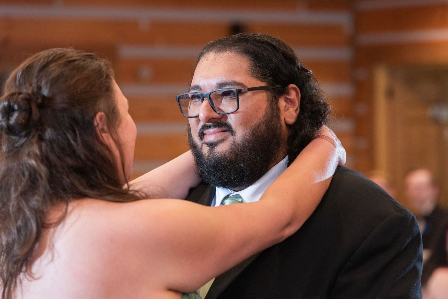 Groom with glasses and beard sharing tender first dance moment with bride in rustic wedding venue.