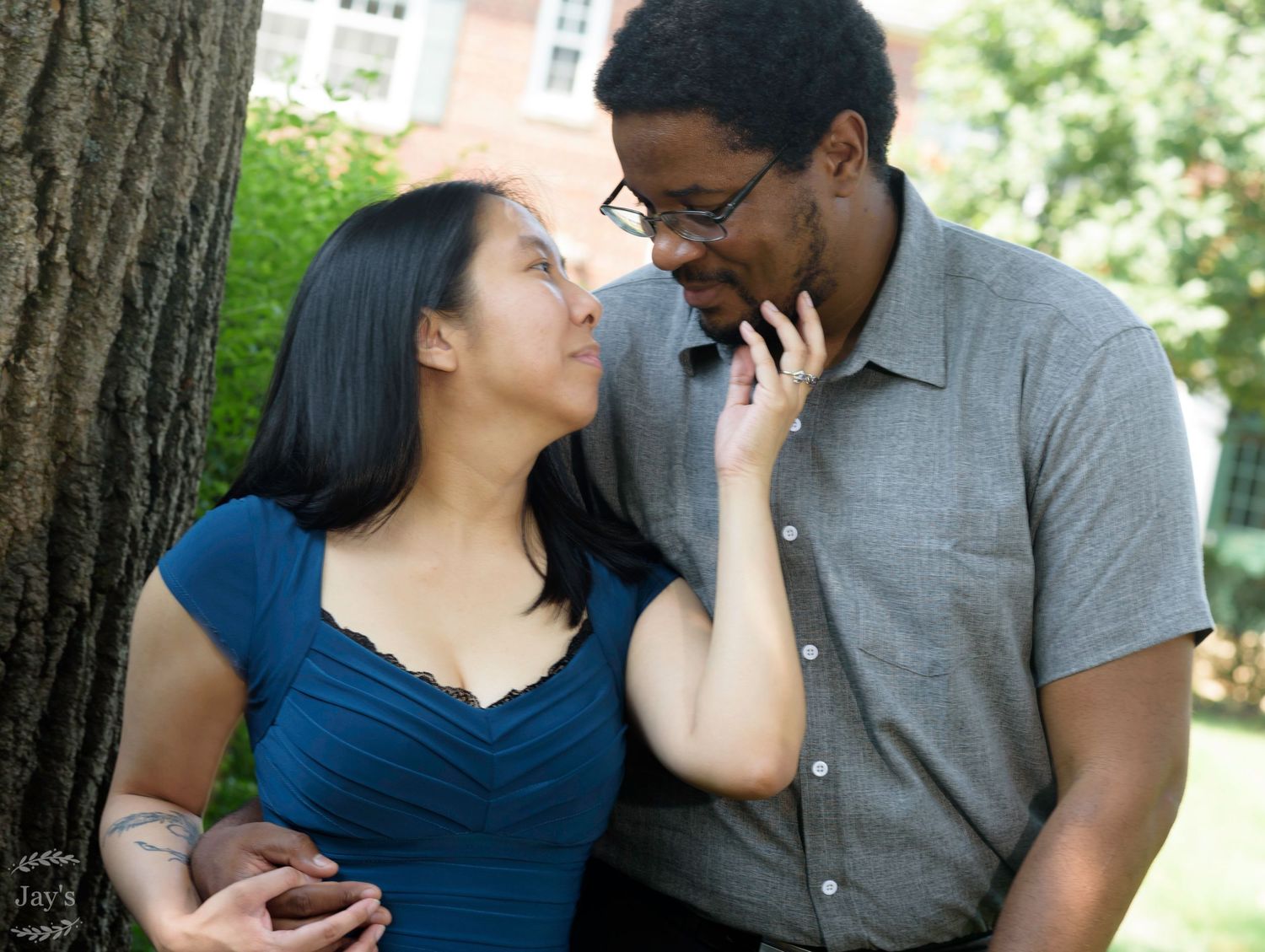Couple smiling at each other tenderly near a tree outdoors.