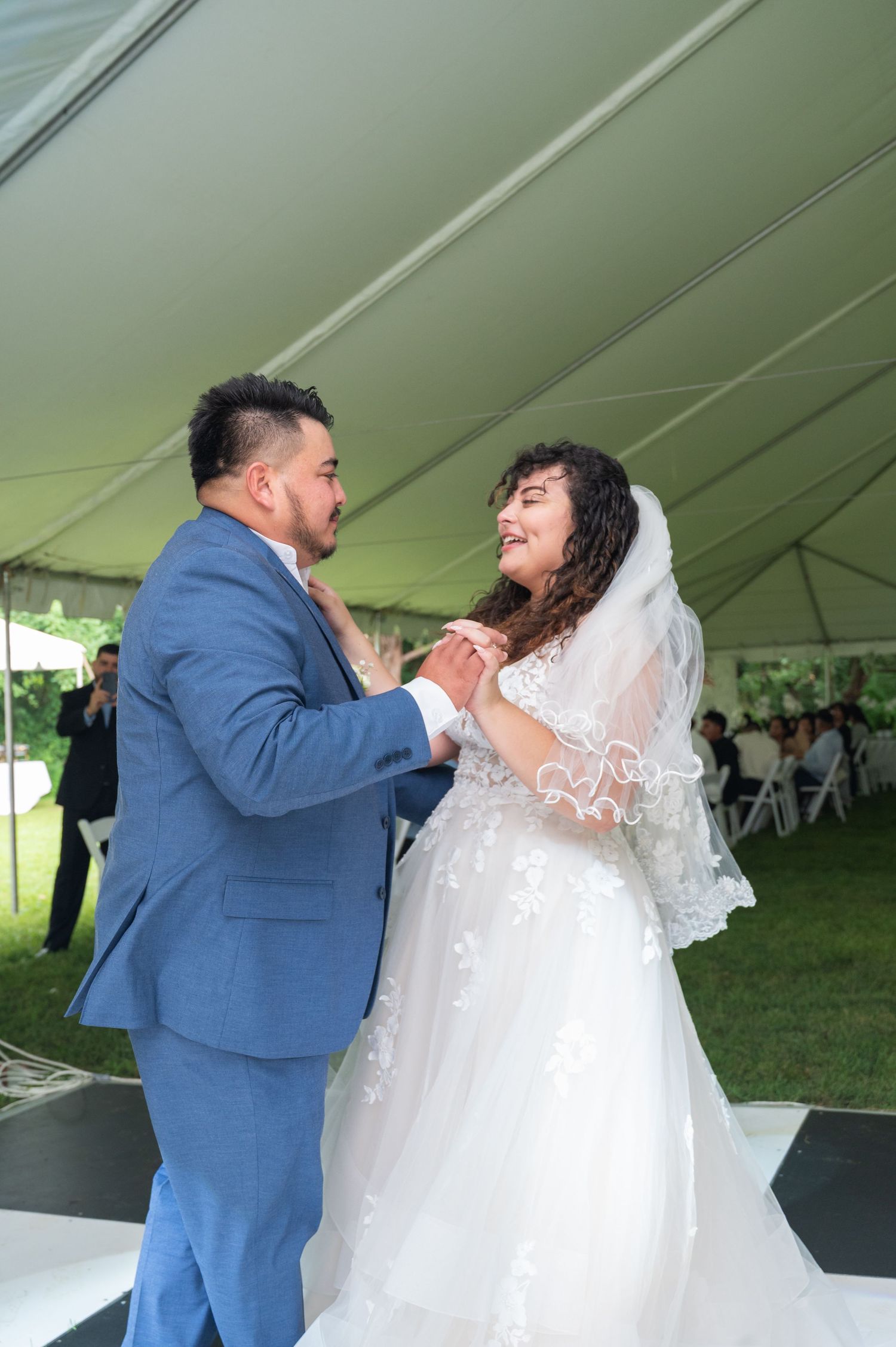 Newlyweds sharing first dance under white tent at elegant outdoor wedding reception.