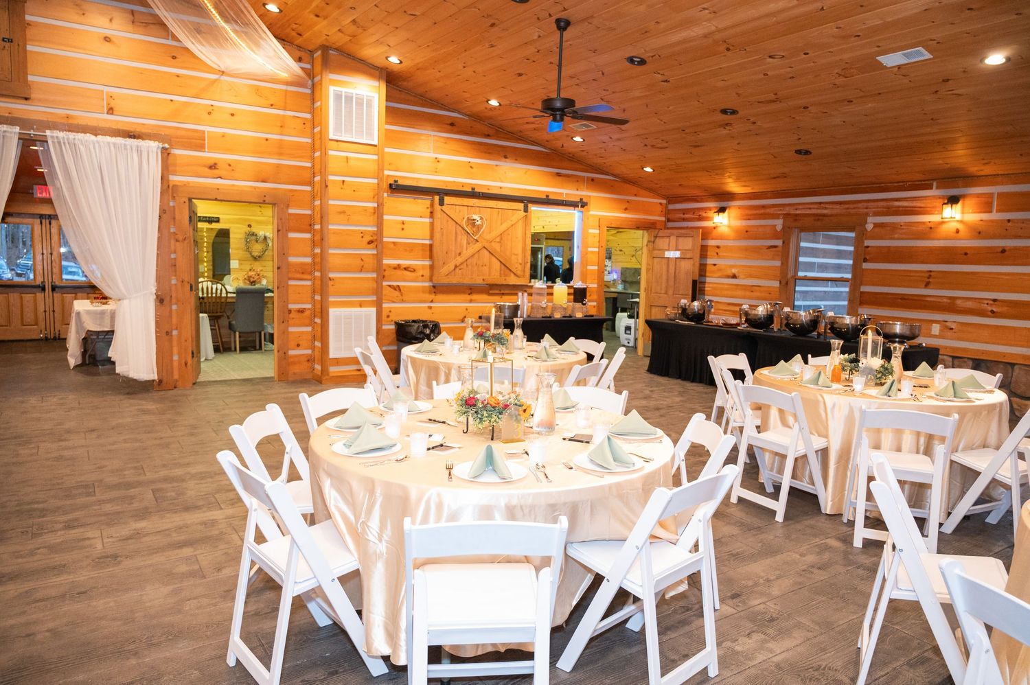 Elegant rustic wedding reception hall with log cabin walls, round tables, and white folding chairs.