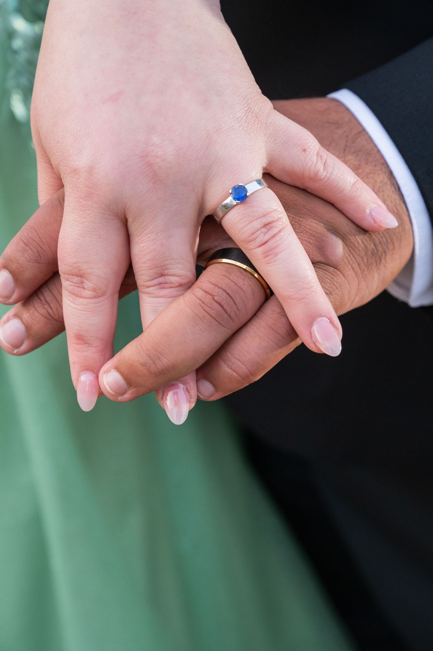Close-up of couple holding hands showing blue sapphire engagement ring and wedding band.