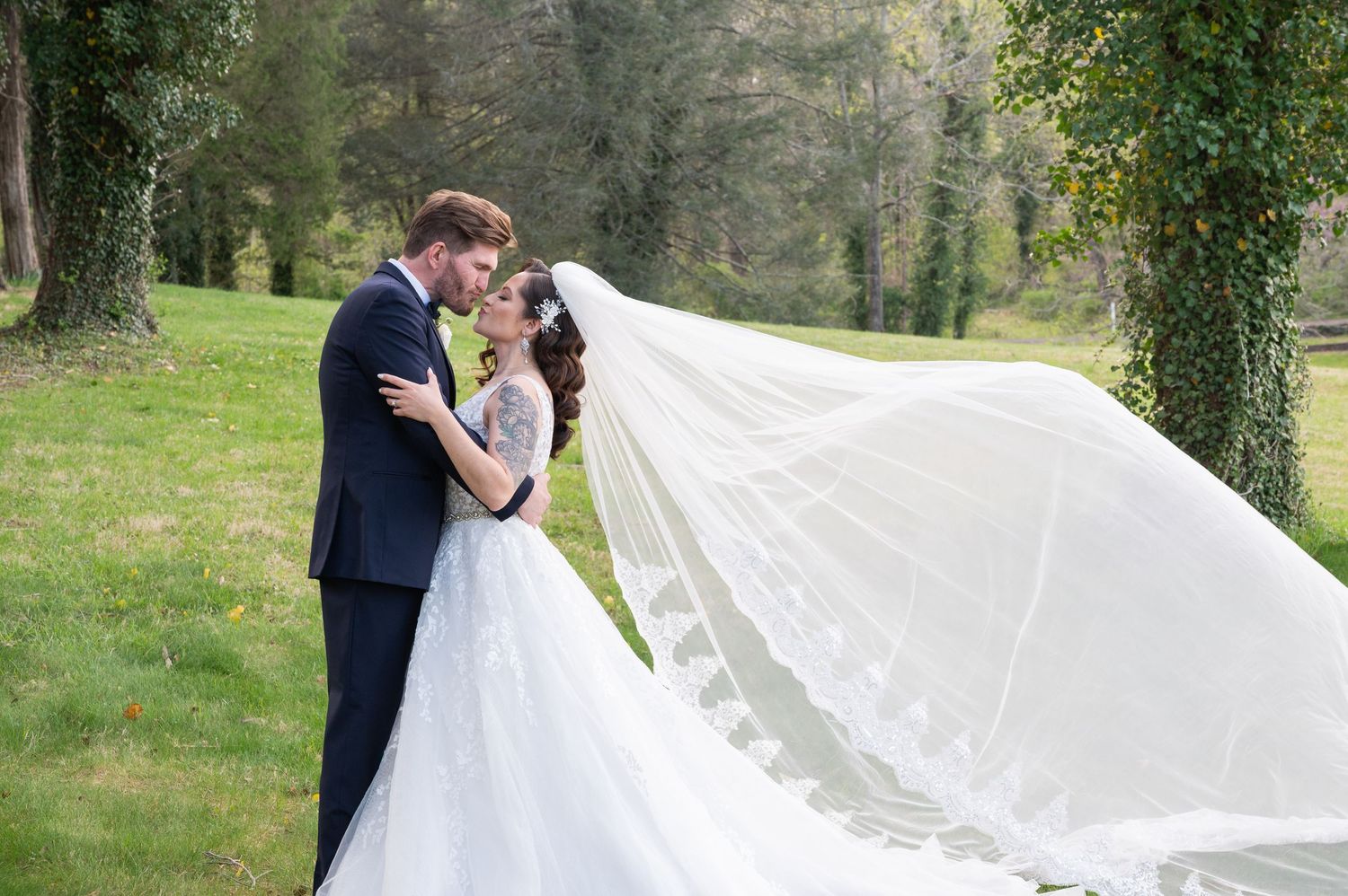 Bride and groom share a romantic moment outdoors as her long white veil billows in the wind.