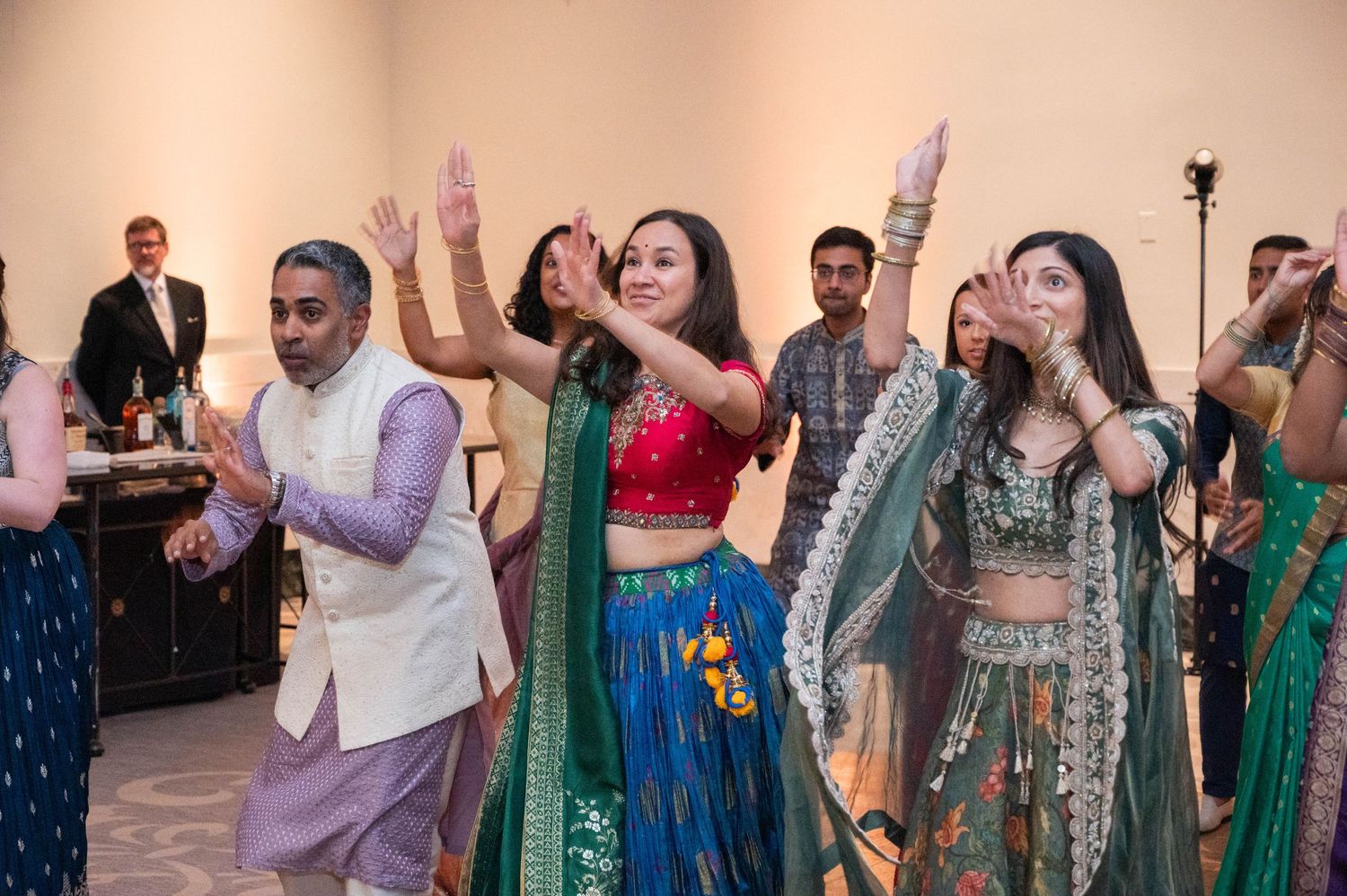 Group of women in colorful Indian attire dancing joyfully at a traditional cultural celebration.