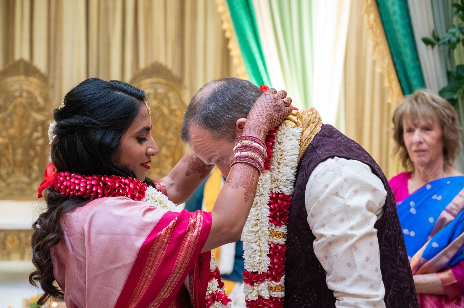 Indian bride placing red and white floral garland around groom's neck during traditional Hindu wedding ceremony.
