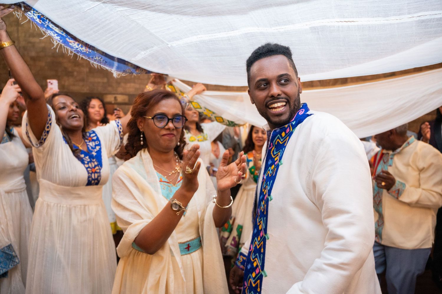Joyful man in white Ethiopian cultural outfit celebrating with guests at a festive event.