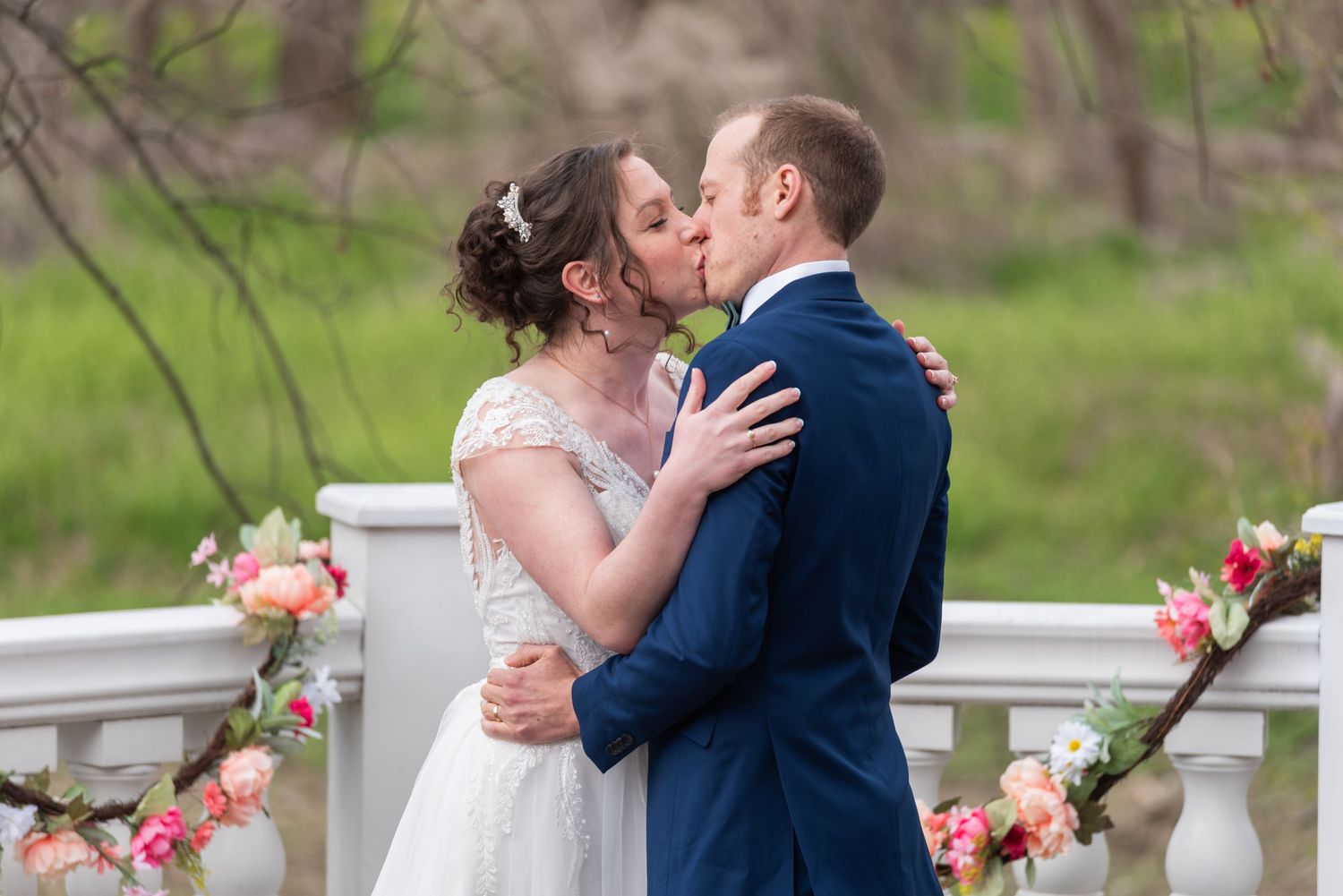 Bride and groom share a first kiss on a floral-decorated white balcony during their ceremony.