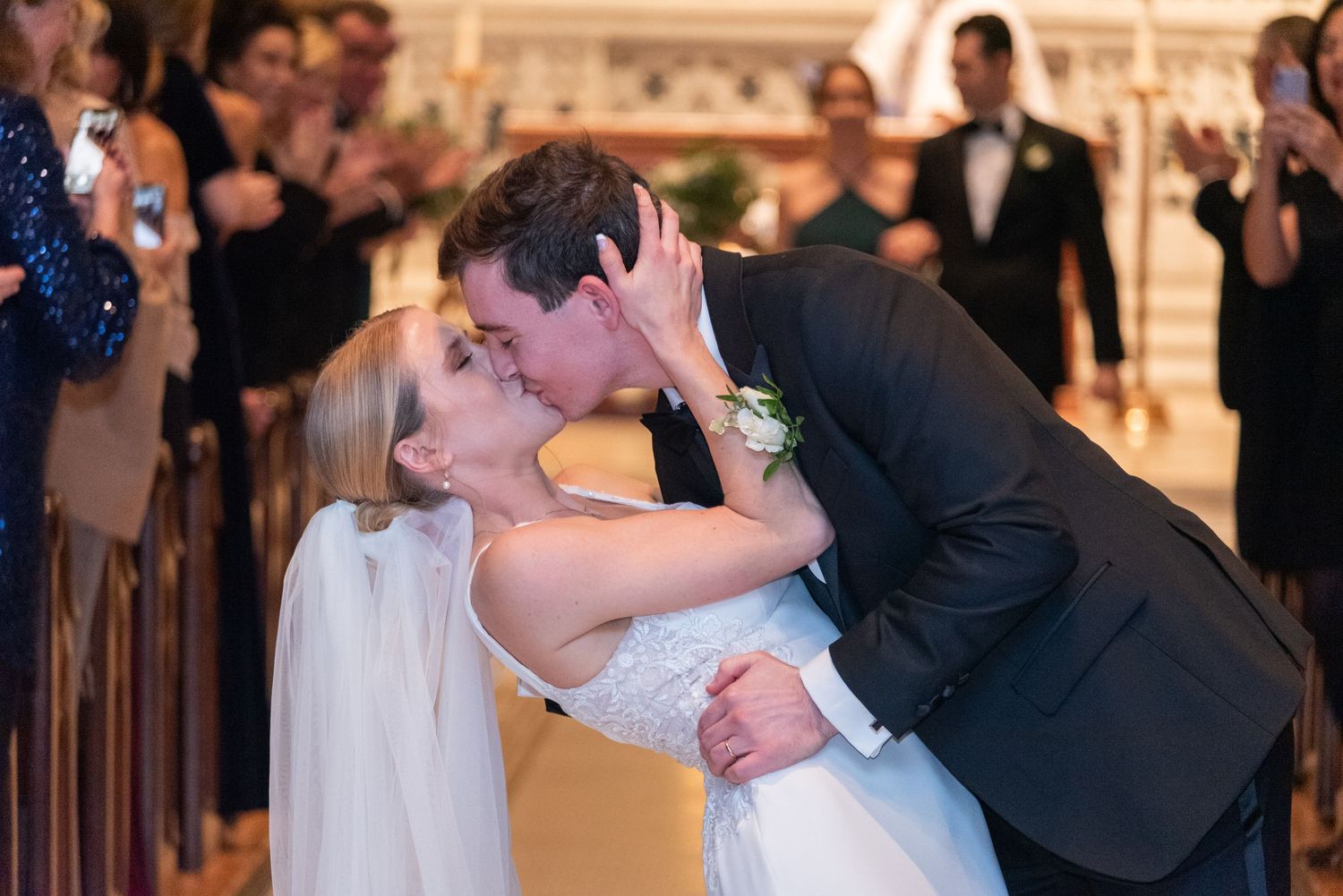 Bride and groom share their first kiss as newlyweds while guests celebrate around them.