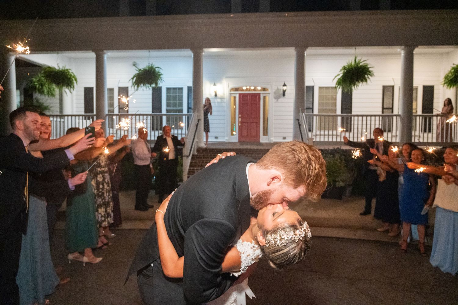 Newlyweds share romantic dip kiss during sparkler send-off at night wedding reception.