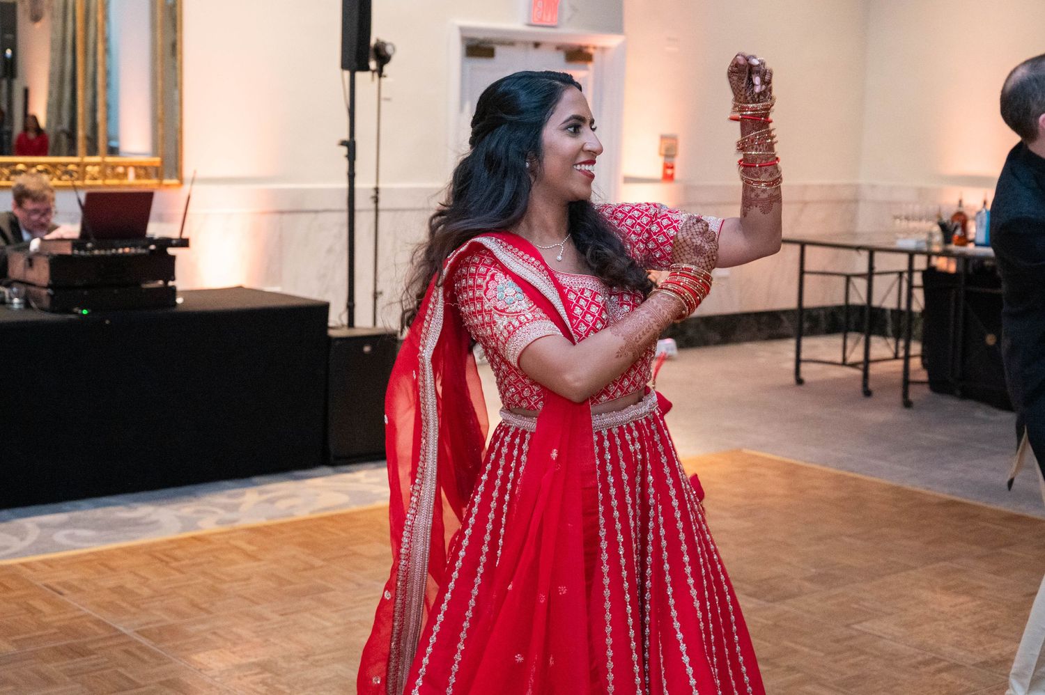 Woman in red lehenga dancing gracefully at an Indian wedding celebration.