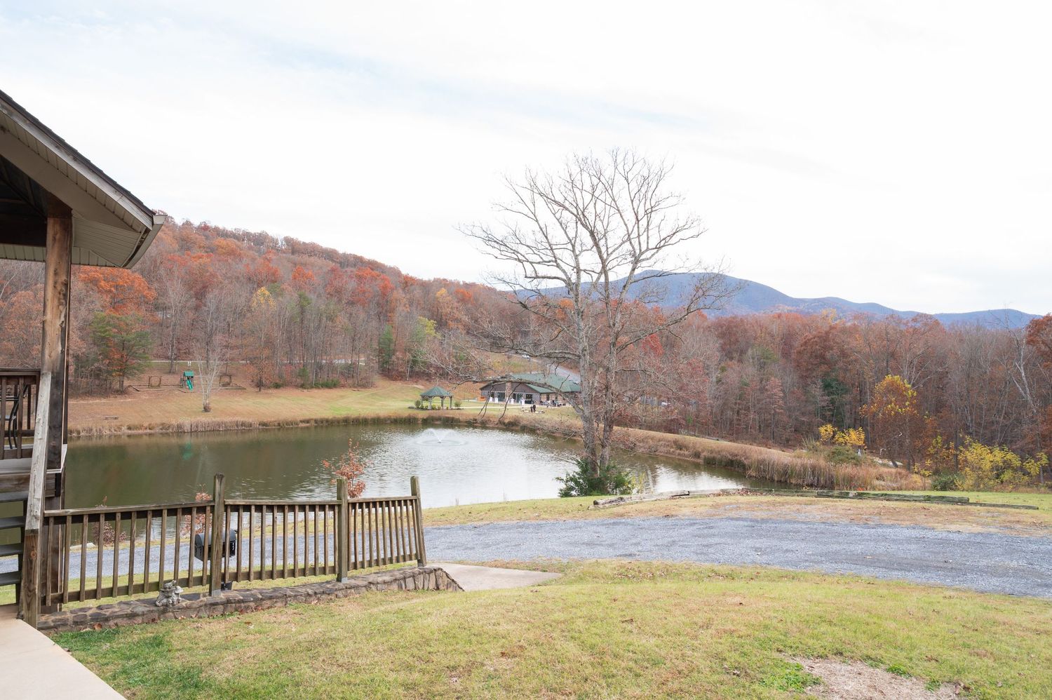 Scenic autumn mountain landscape with a tranquil pond, colorful fall foliage, and a wooden deck overlooking the serene countryside.