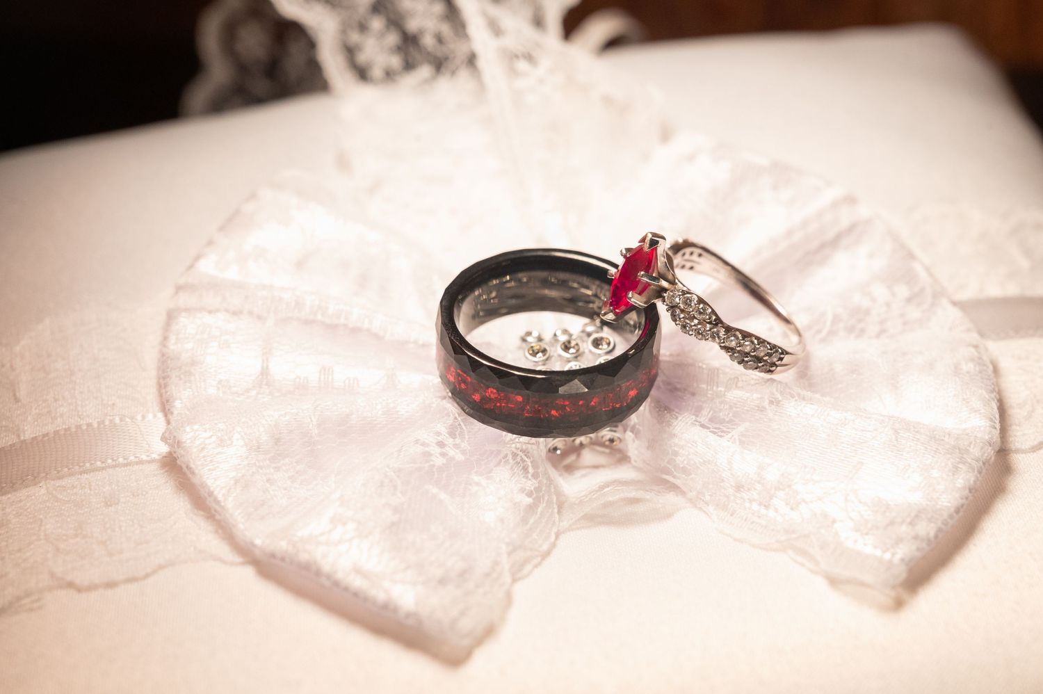 Ruby engagement ring and black wood wedding band on white lace pillow.