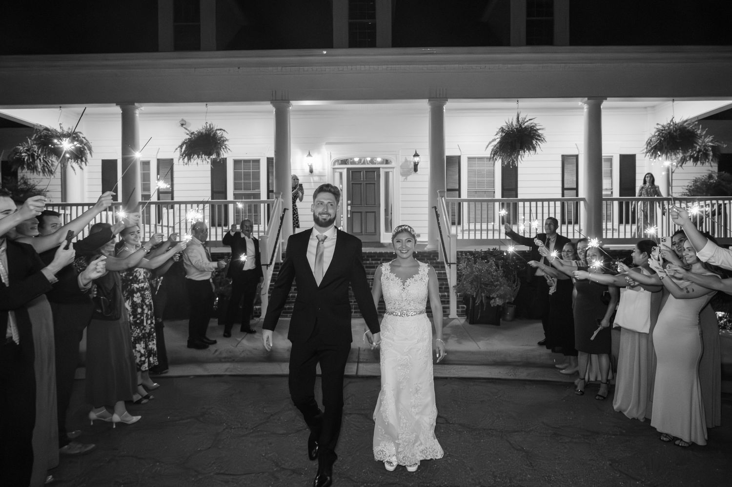 Bride and groom exit wedding reception through sparkler send-off at elegant Southern plantation venue at night.