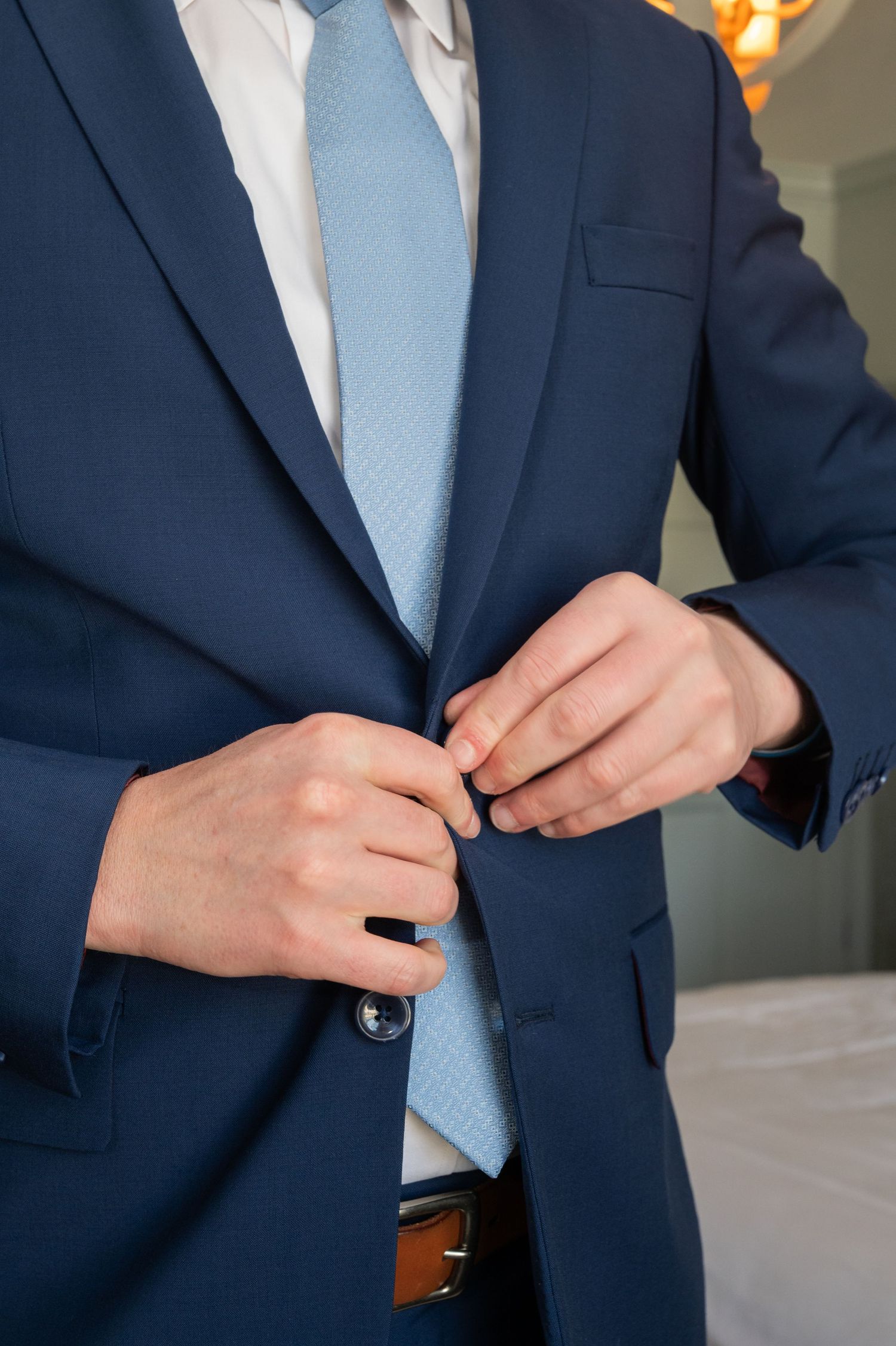 Groom buttoning his navy blue suit jacket with a light blue tie on his wedding day.