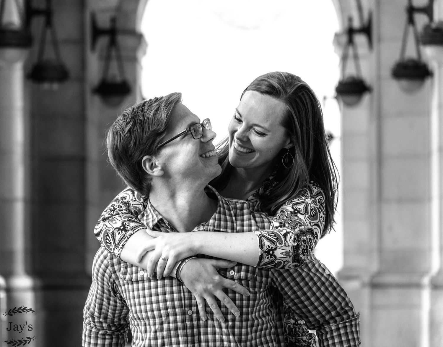 Black and white photo of a laughing couple embracing outdoors near stone archways.