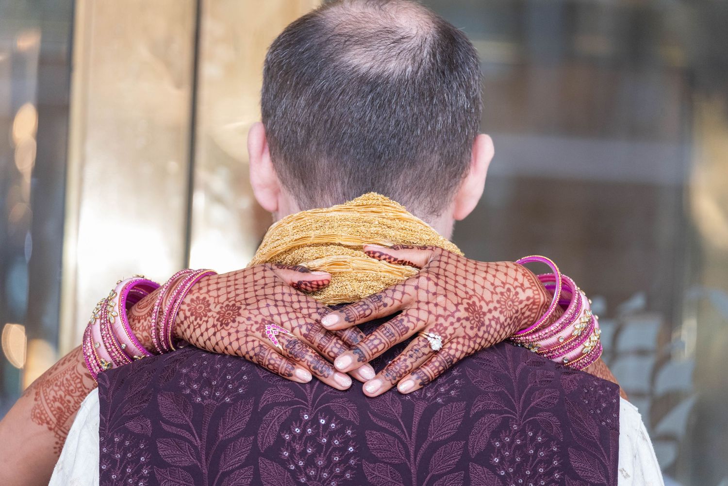 Woman with henna mehndi hands and bangles embracing a man from behind at an Indian wedding ceremony.