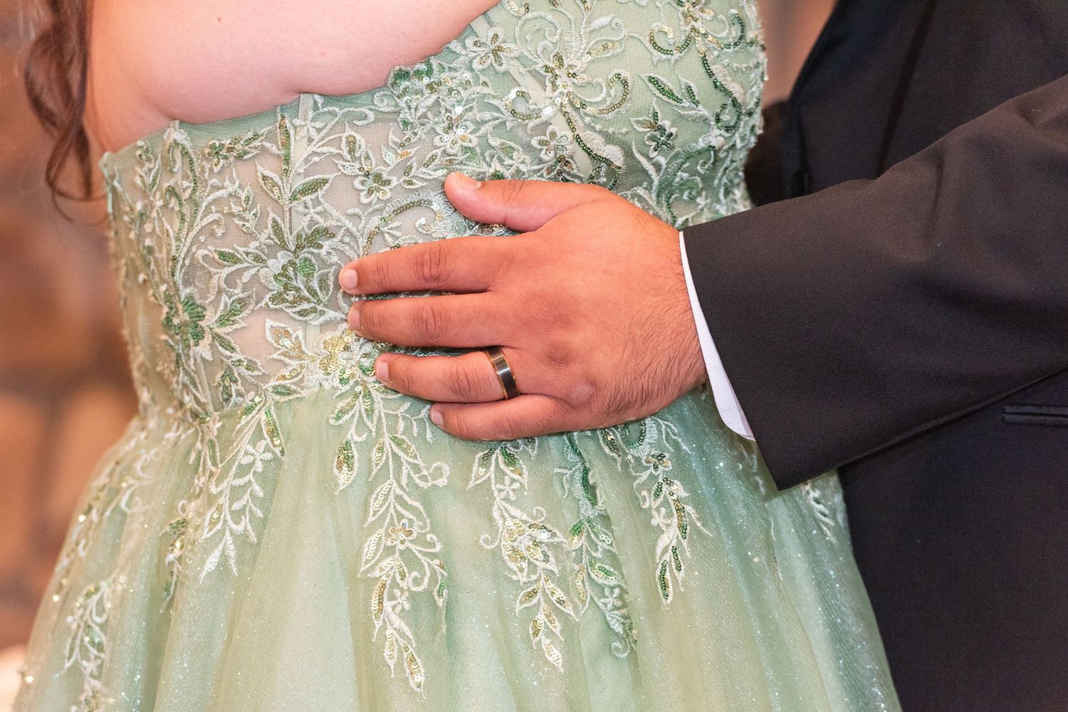 Close-up of groom's hand with wedding band resting on bride's mint green lace wedding gown.