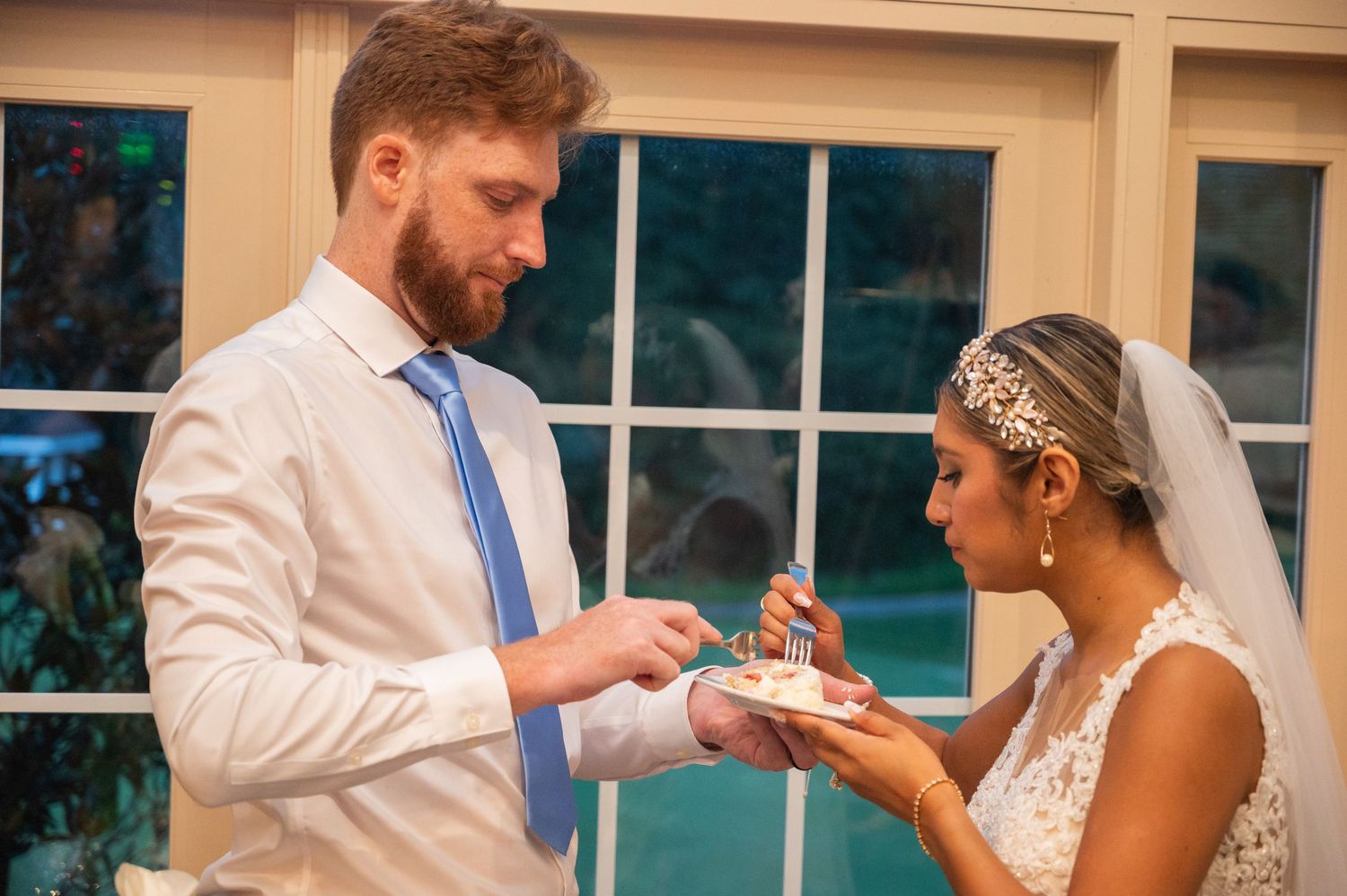 Groom places wedding ring on bride's finger during intimate indoor ceremony near sunlit windows.