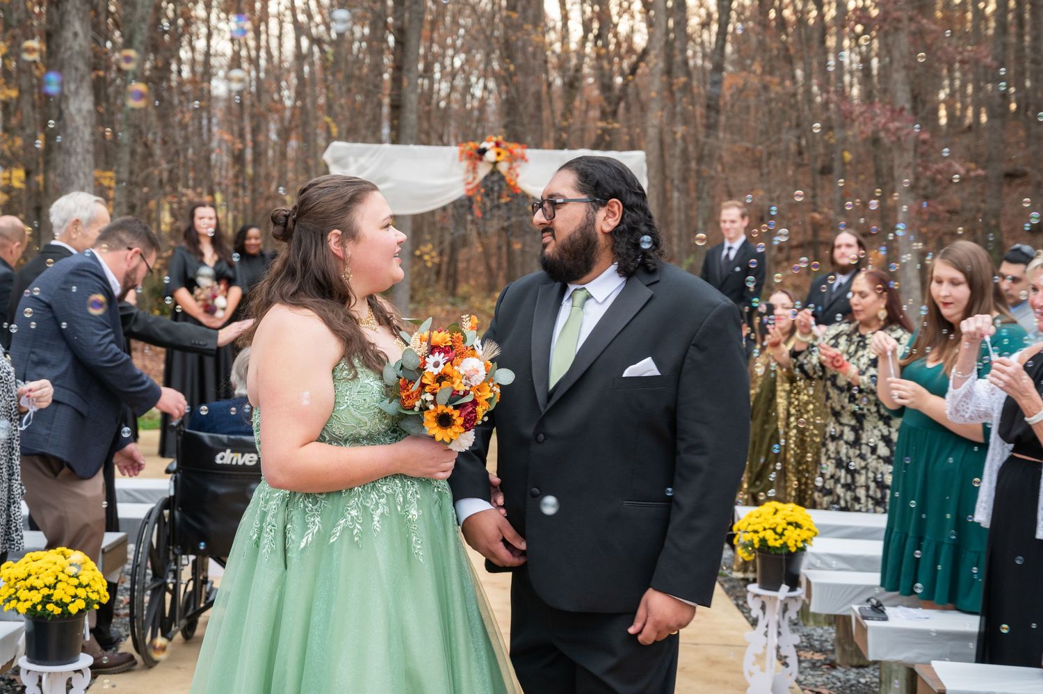 Newlyweds share joyful moment walking down aisle as guests celebrate with confetti at outdoor fall wedding.