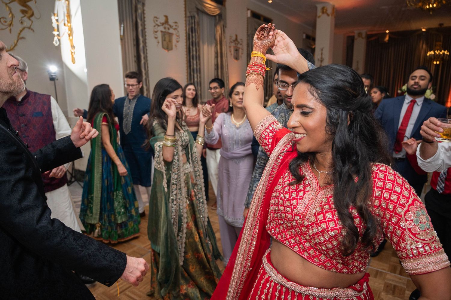 Indian bride in red lehenga spinning joyfully on the dance floor at wedding reception.