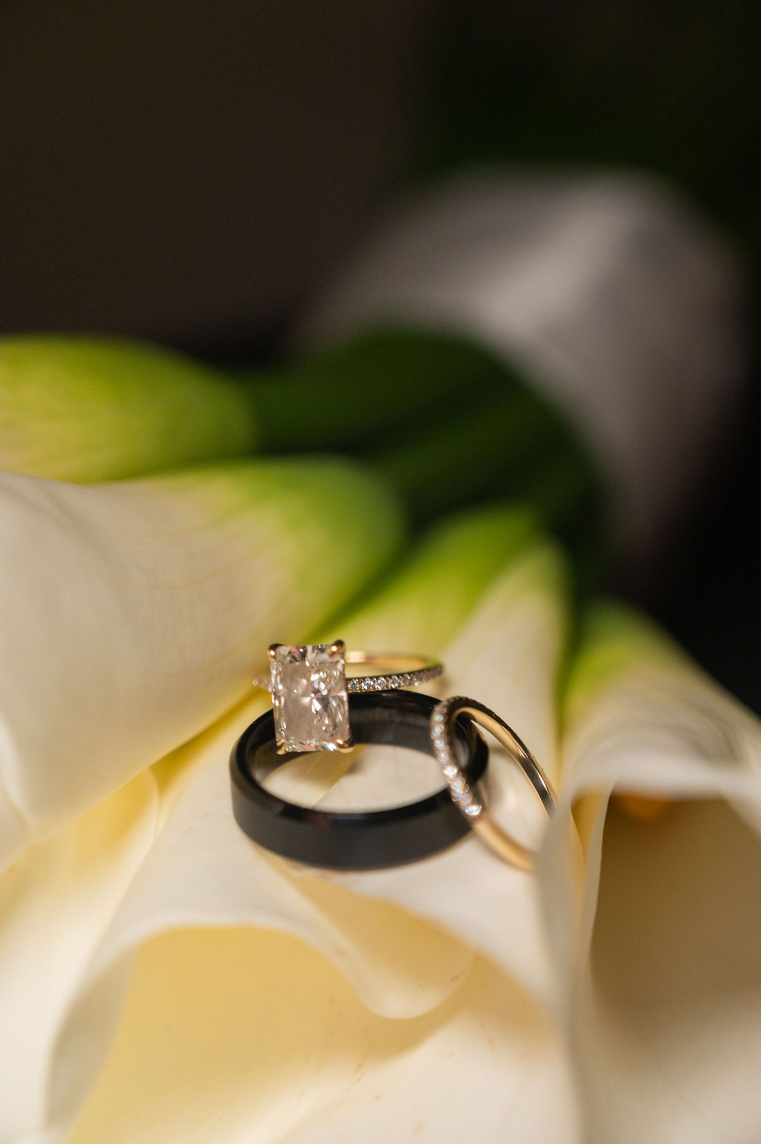 Diamond engagement ring and black wedding band displayed on a white calla lily flower.