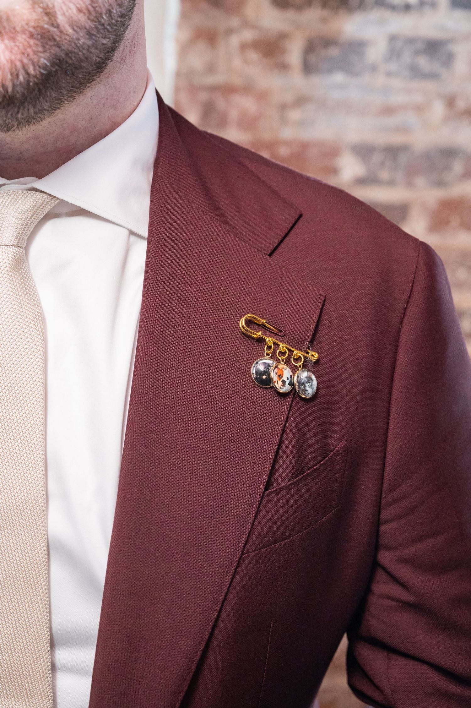Groom in burgundy suit with cream tie wearing a unique gold pin boutonniere.