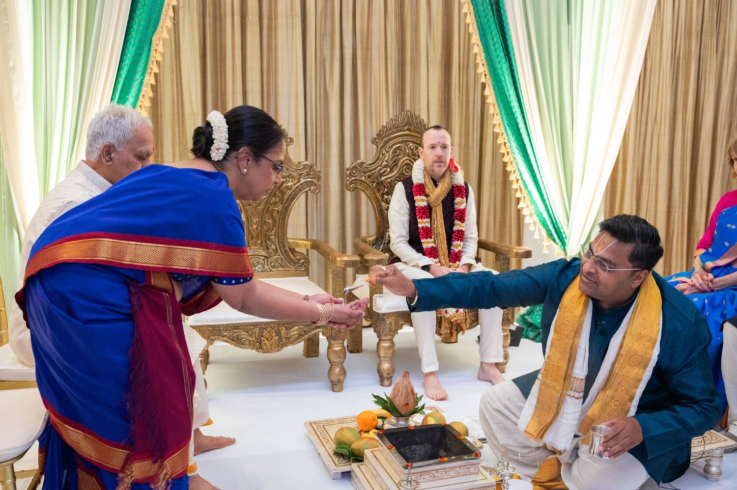 Indian wedding ceremony with guests in colorful traditional attire gathered around a sacred fire ritual mandap.