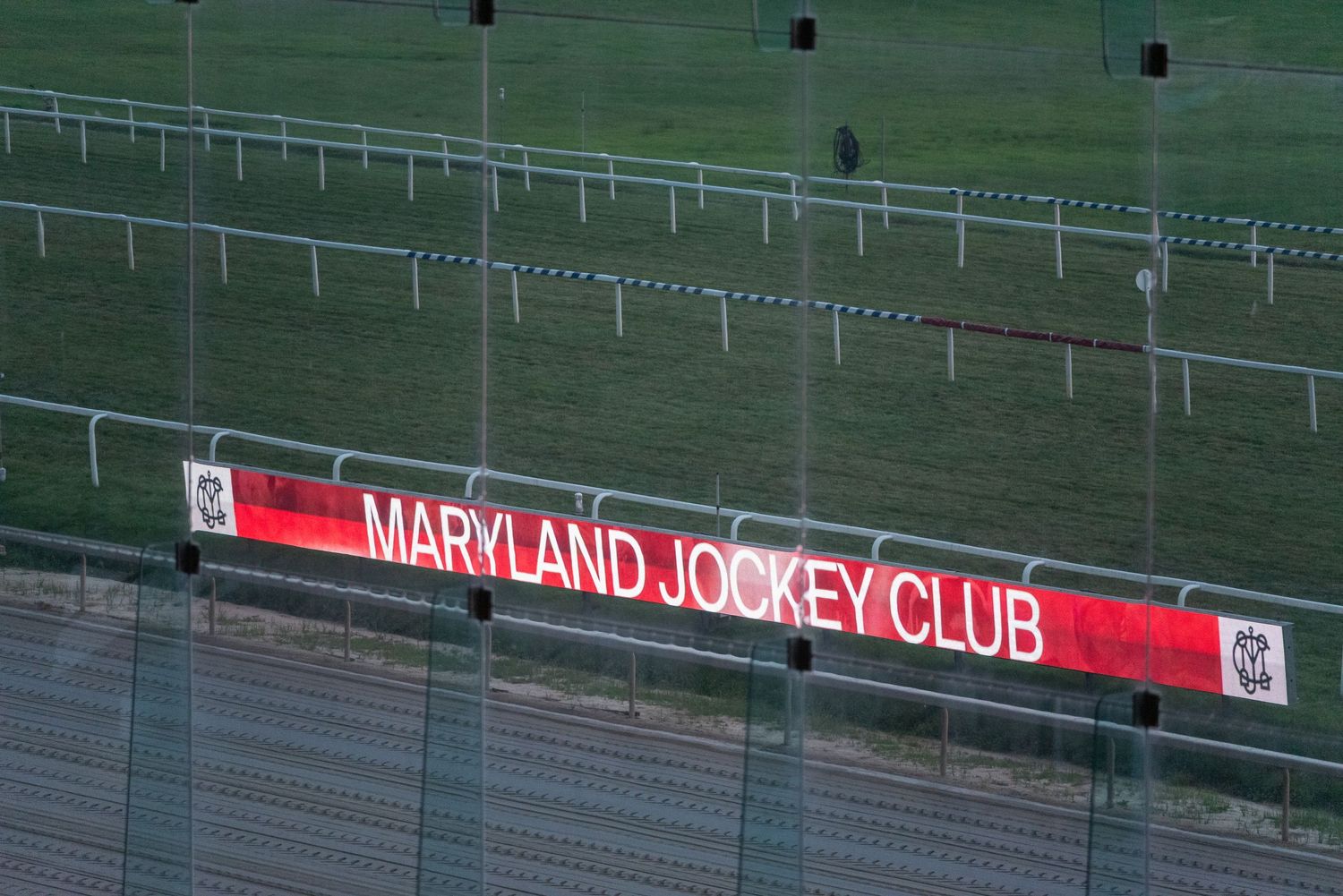 Maryland Jockey Club illuminated red sign at a horse racing track with green turf and white rail fences.