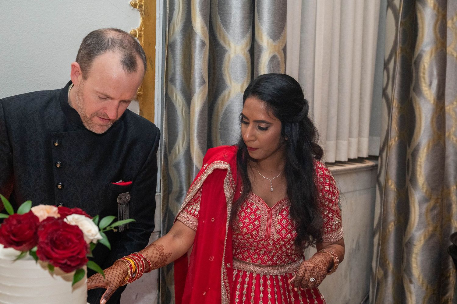 Bride in red lehenga and groom in black sherwani together during wedding reception.