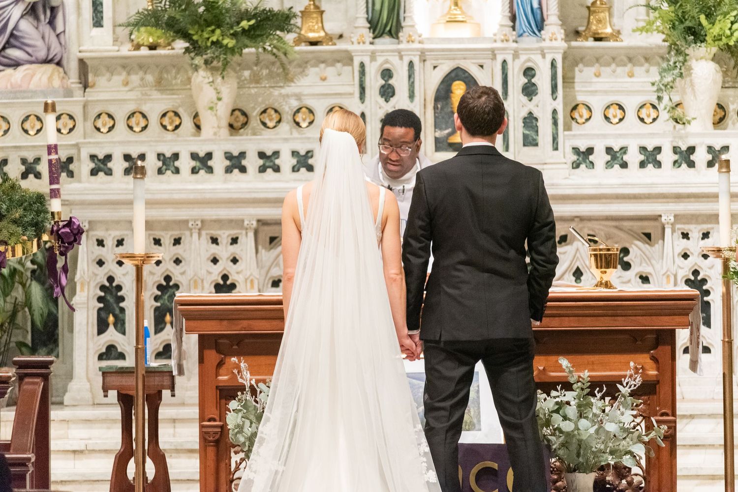 Bride and groom stand at the altar of an ornate church during their wedding ceremony.