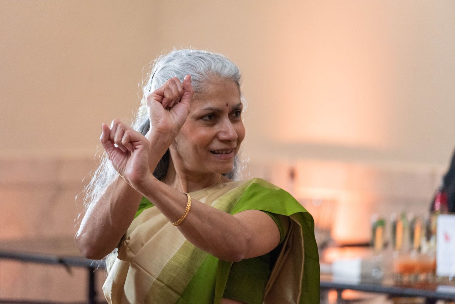 Elderly Indian woman in green saree dancing gracefully with raised fist at a celebration.